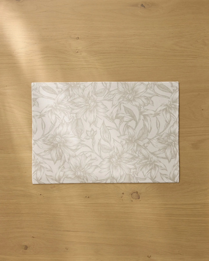 The Geometry Alba rectangular white recycled placemat, featuring a subtle floral pattern, rests on a light wooden table bathed in soft natural light.