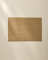 The Amber Stitch placemat by Geometry features a rectangular brown design with a small white cross pattern, lying flat on a light beige surface. Soft natural light highlights its style—machine washable and perfect for inviting table settings.