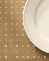 The Geometry Amber Stitch placemat, stylish and machine washable, perfectly complements a white scalloped ceramic plate on a tan tablecloth with small white cross designs.