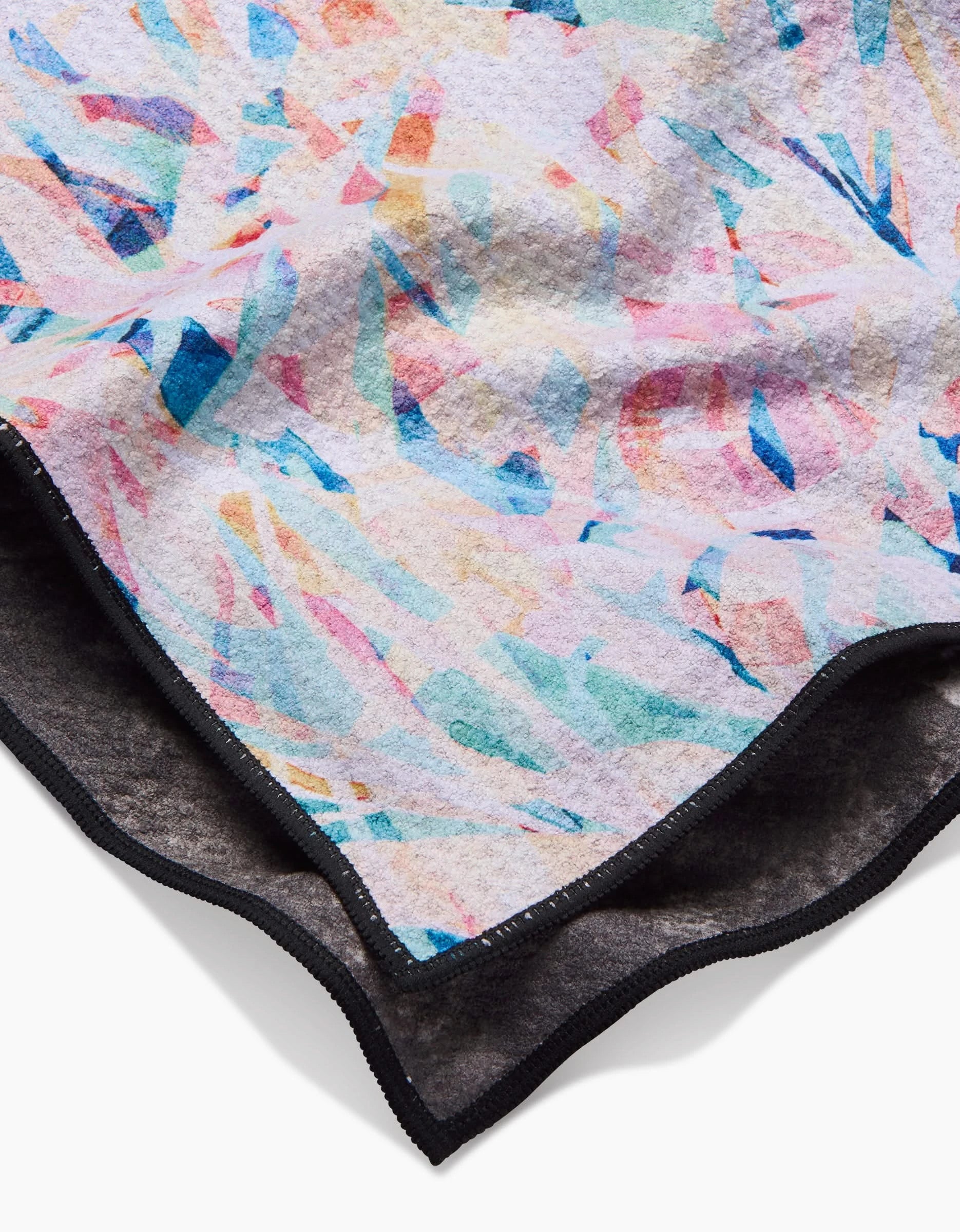 A close-up of the Abstract Jungle blanket by Rachel Parker, featuring soft Geoweave fabric with a pastel abstract watercolor pattern in pink, blue, and yellow, a black border, and a corner folded to show the ultra-absorbent dark underside.