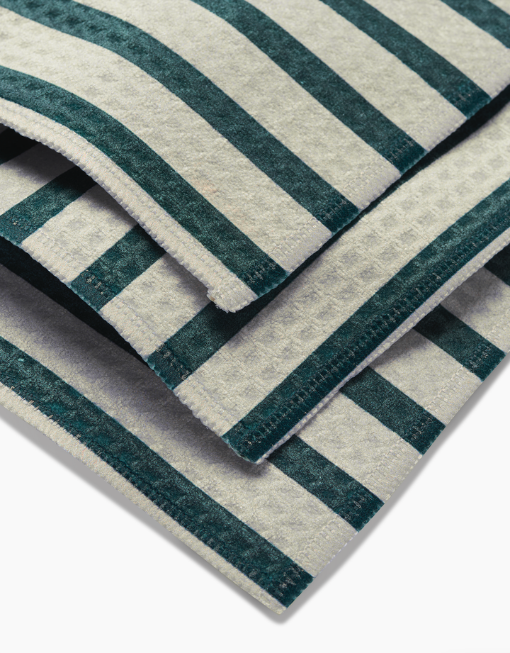 A close-up of GEOMETRY Deep Green Stripes washcloths shows their green and white striped pattern, detailed fabric texture, and Geoweave-crafted edges, all set against a white background.