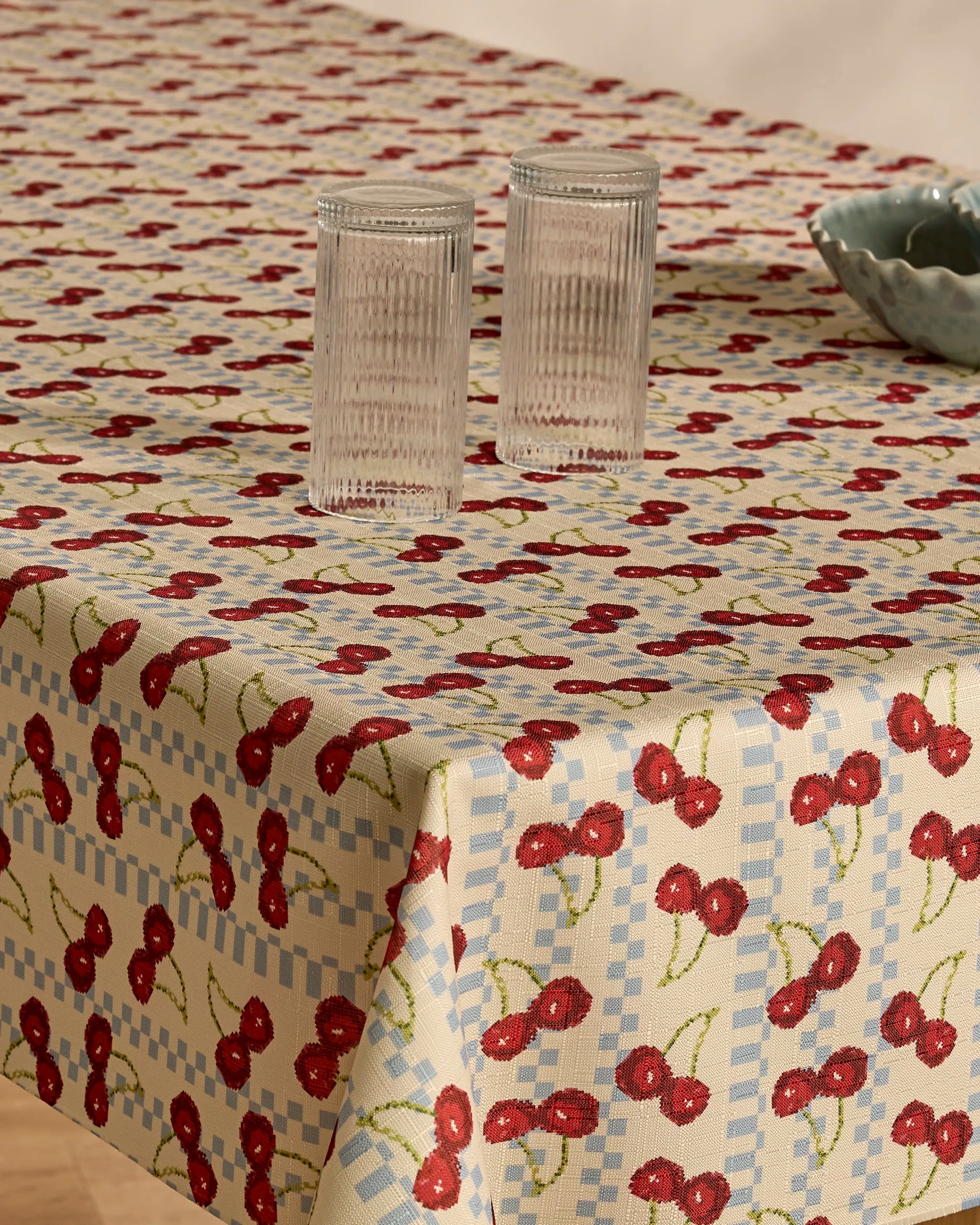 A table topped with Geometry’s Cherry Cola spill-resistant tablecloth, adorned with two clear ribbed glass tumblers and a blue ceramic bowl.