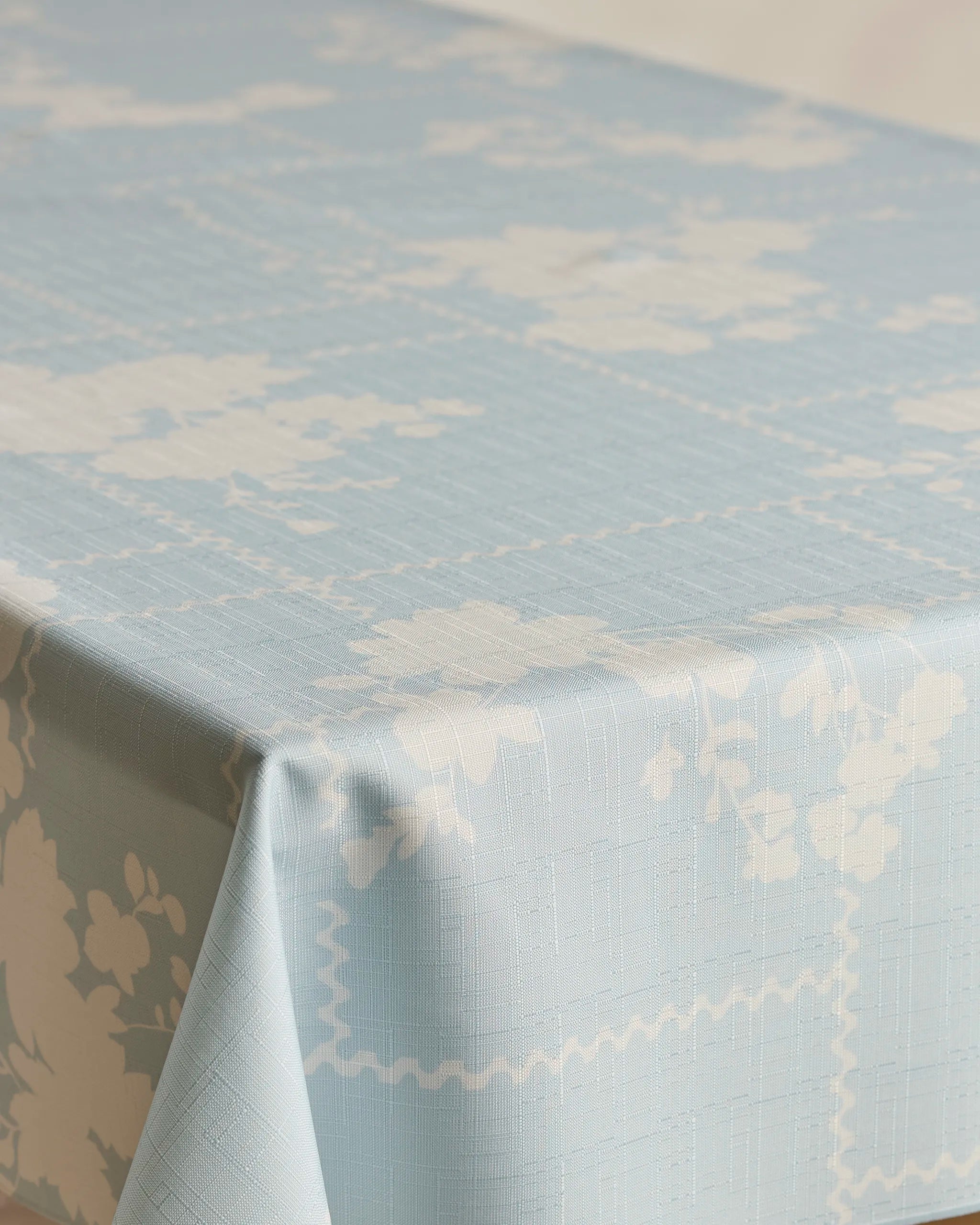 The Floral Whispers tablecloth by Geometry, in light blue with a subtle white floral and geometric pattern, adds spill-resistant elegance to any rectangular table.