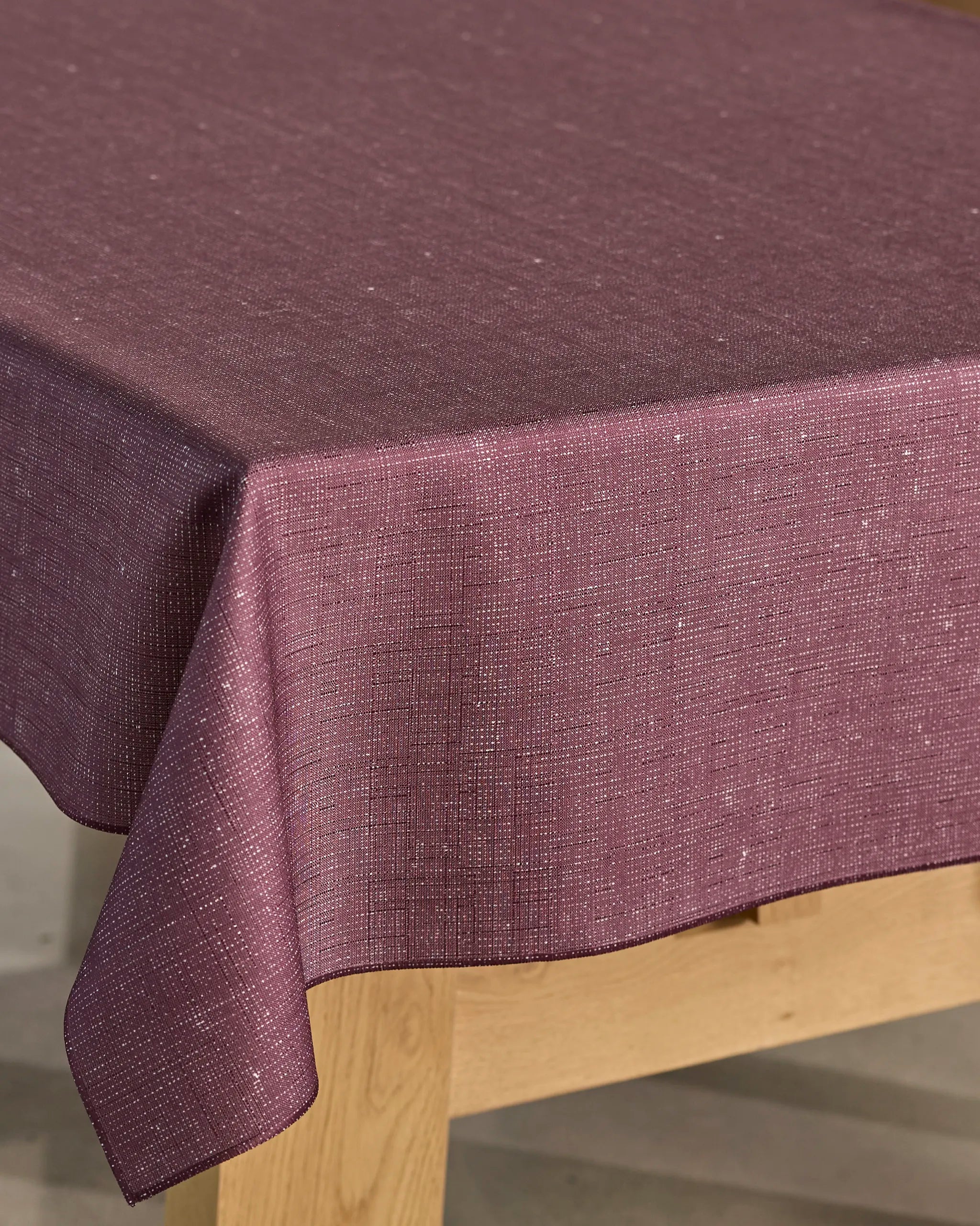 A close-up of Geometry’s Gather tablecloth, in textured dark mauve, drapes neatly over a wooden table and features a subtle woven pattern plus spill-resistant finish.