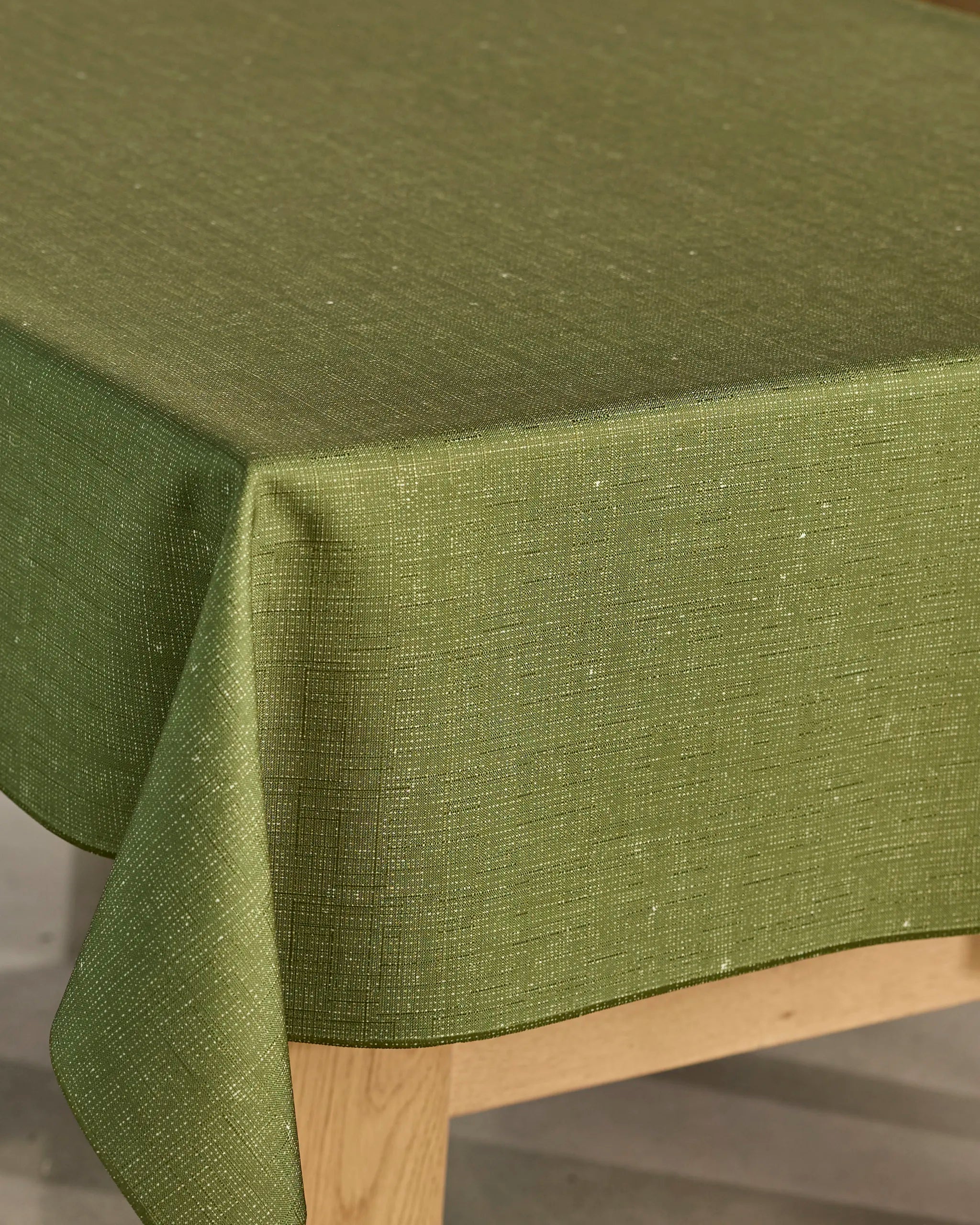 A close-up of a wooden table covered with Geometry’s Gather tablecloth in textured green, featuring spill-resistant fabric and neatly draped edges.