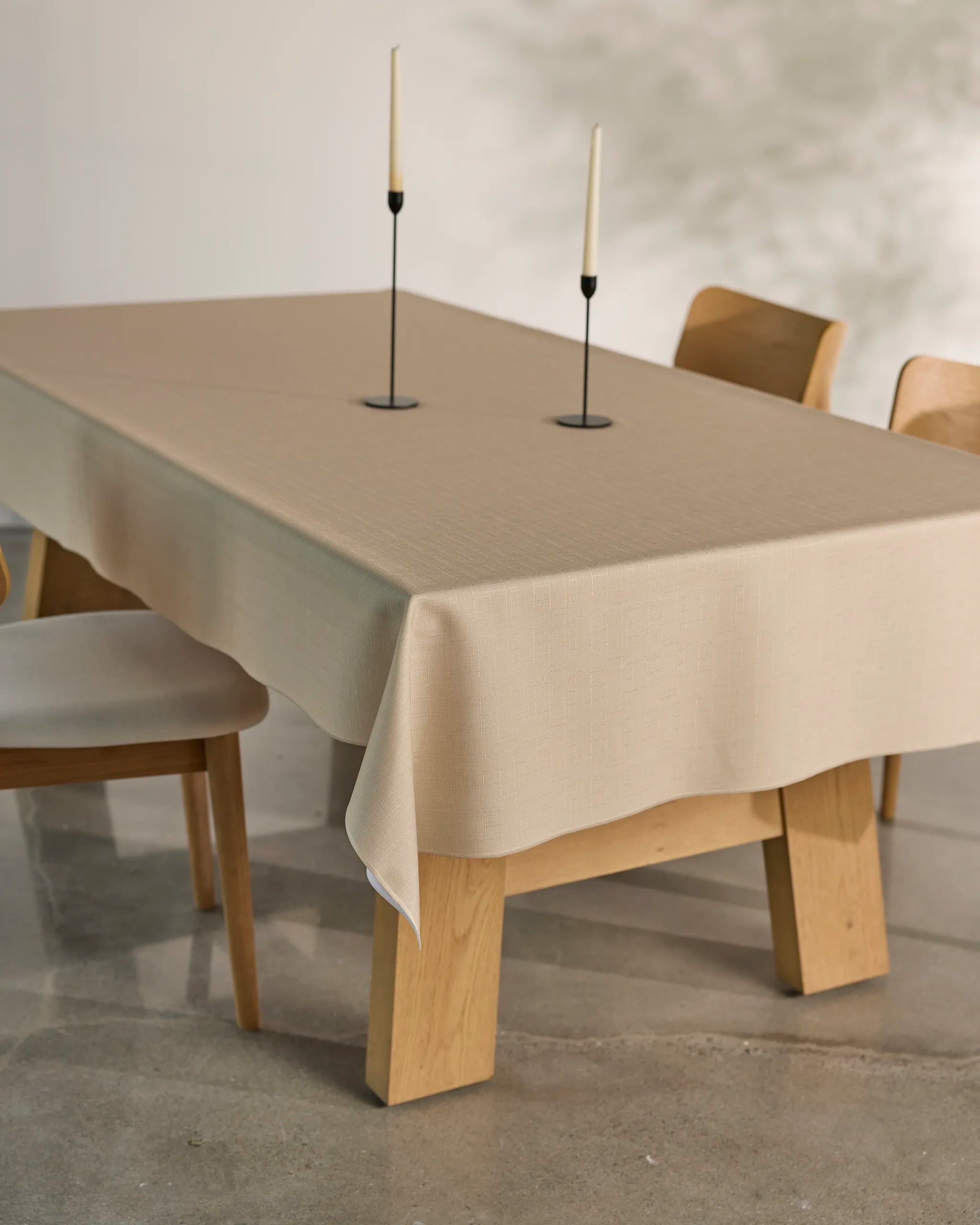 The Geometry Gather dining set features a minimalist table with a spill-resistant cloth, two wooden chairs, and slim white candles in black holders. Set on polished concrete, soft natural light gently highlights the ensemble.