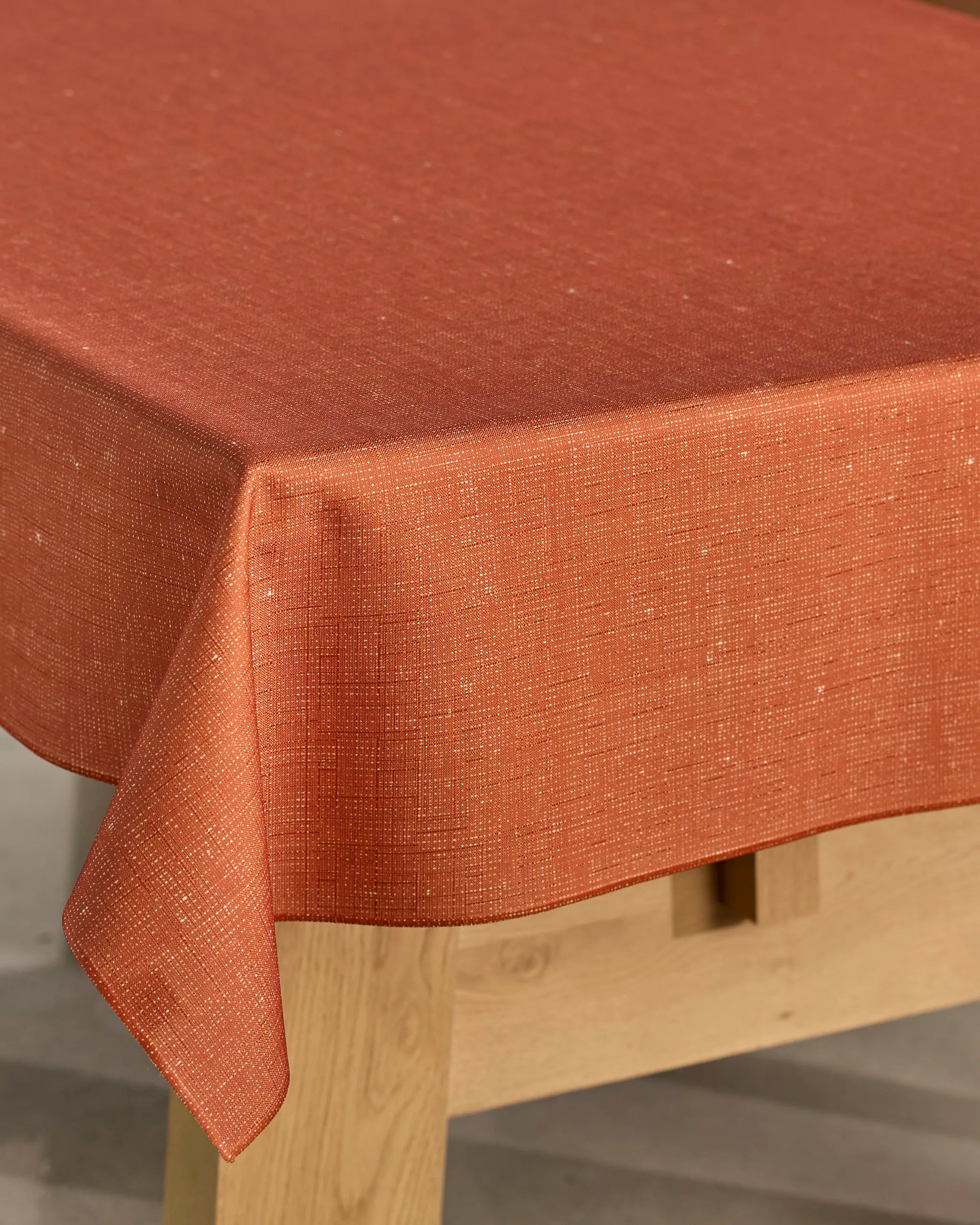 A close-up of a wooden table draped with the Geometry Gather tablecloth, featuring a textured, burnt orange, spill-resistant design that hangs elegantly over the edge.