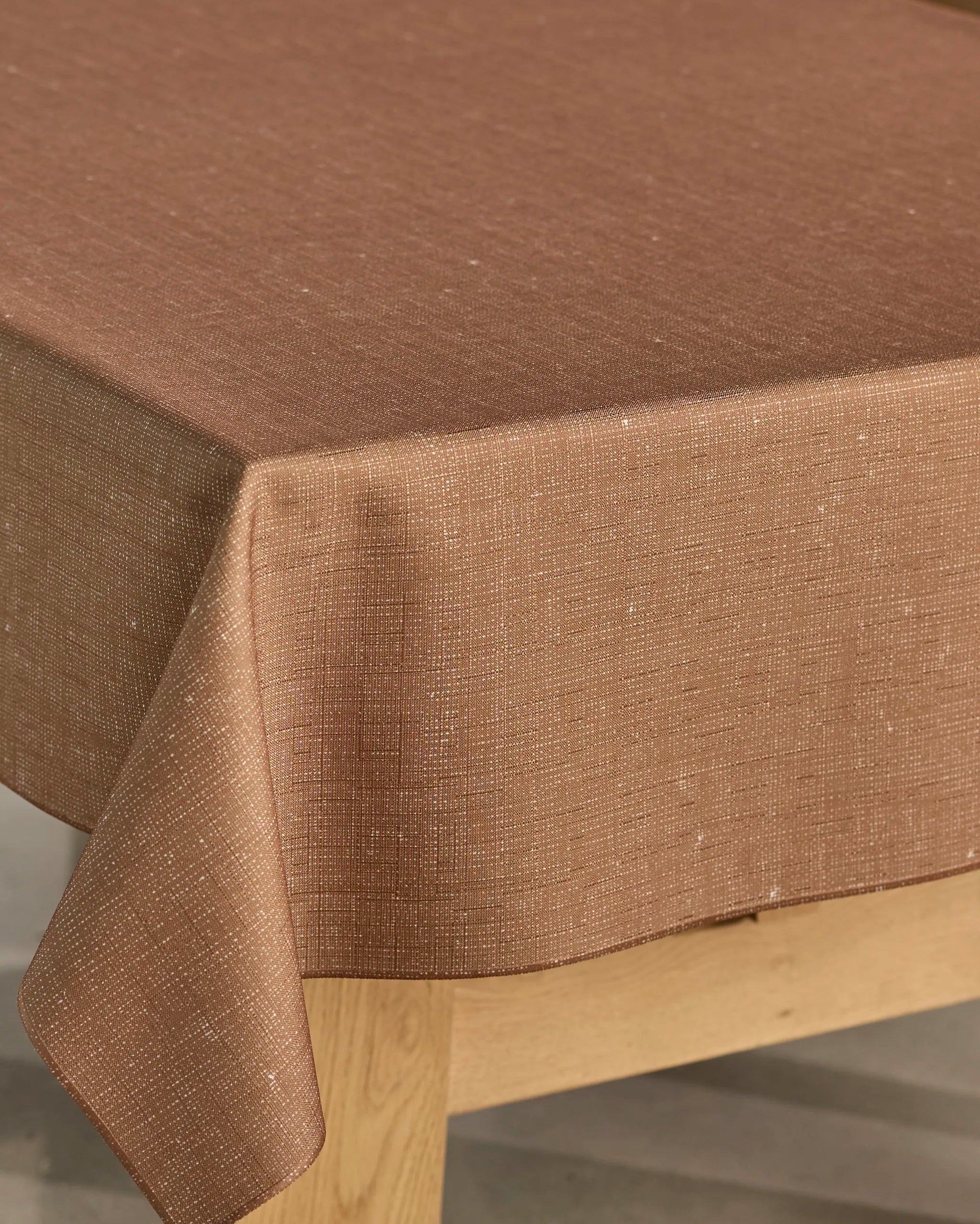 A close-up of Geometry’s Gather rectangular wooden table shows a brown, textured recycled tablecloth neatly draped over the corner.