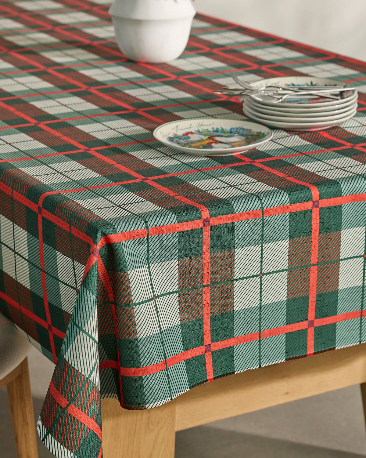 A wooden chair peeks into view as a festive scene unfolds—a table draped in Geometry’s Noel Tartan tablecloth. The vivid red, green, and white plaid design brings holiday cheer, while stacked plates, forks, and a crisp white bowl rest on top. Both stylish and spill-resistant, the Noel Tartan adds practicality to this inviting setting.