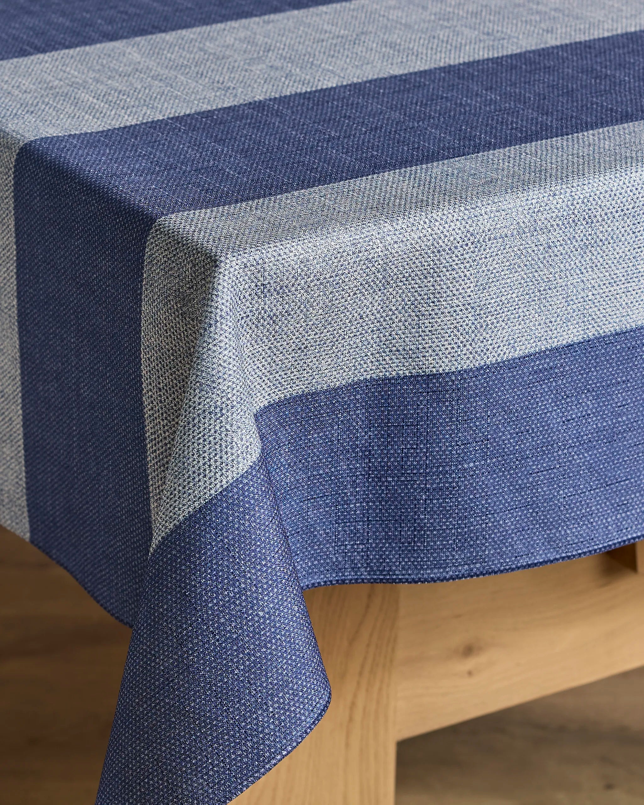 A close-up of a rectangular wooden table featuring Geometry’s Everband tablecloth in blue and light gray stripes, with recycled fabric draped over the edge to showcase its textured pattern.