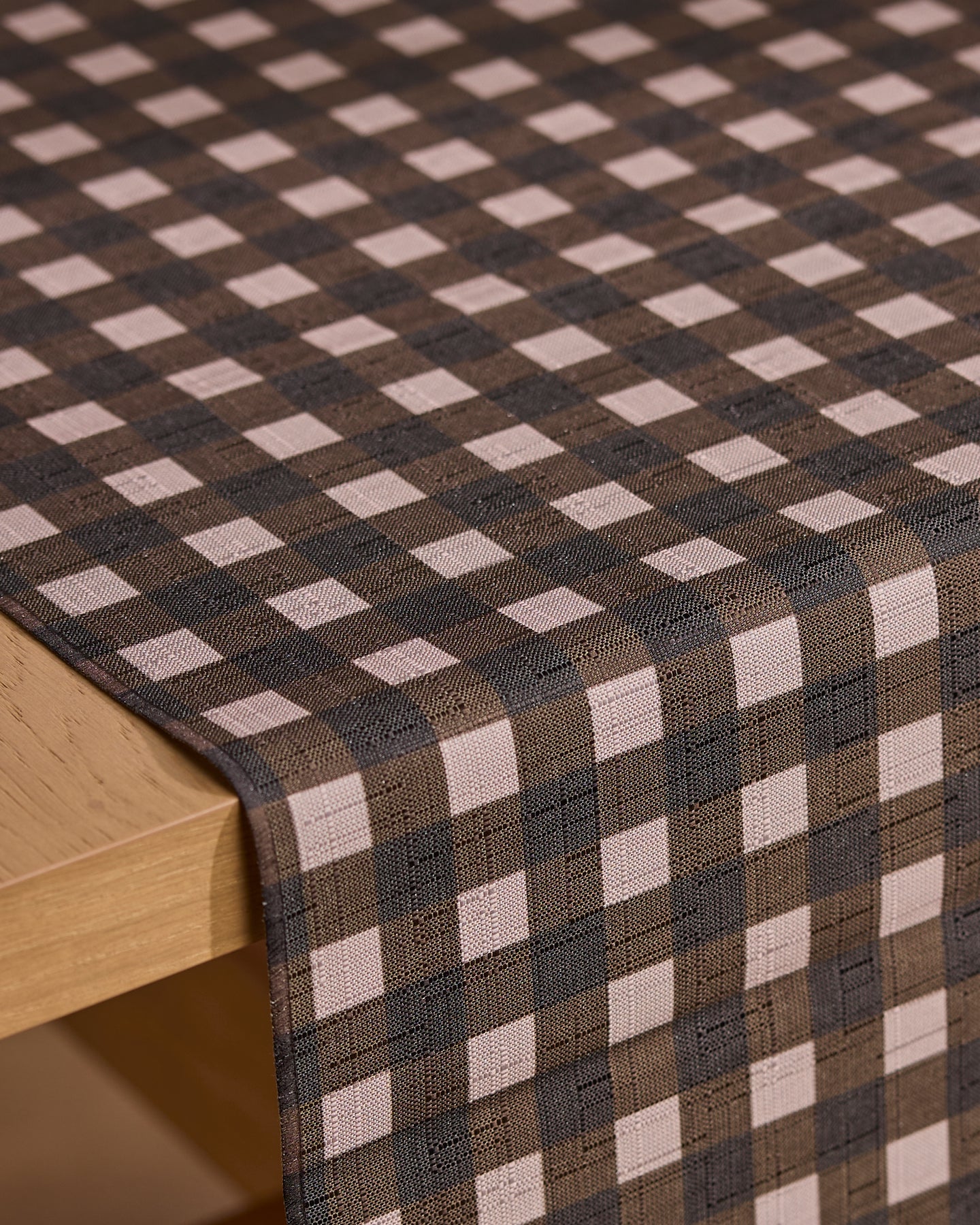 A close-up of a table with the Geometry Deep Hearth brown and beige stain-resistant table runner draped neatly over the edge.