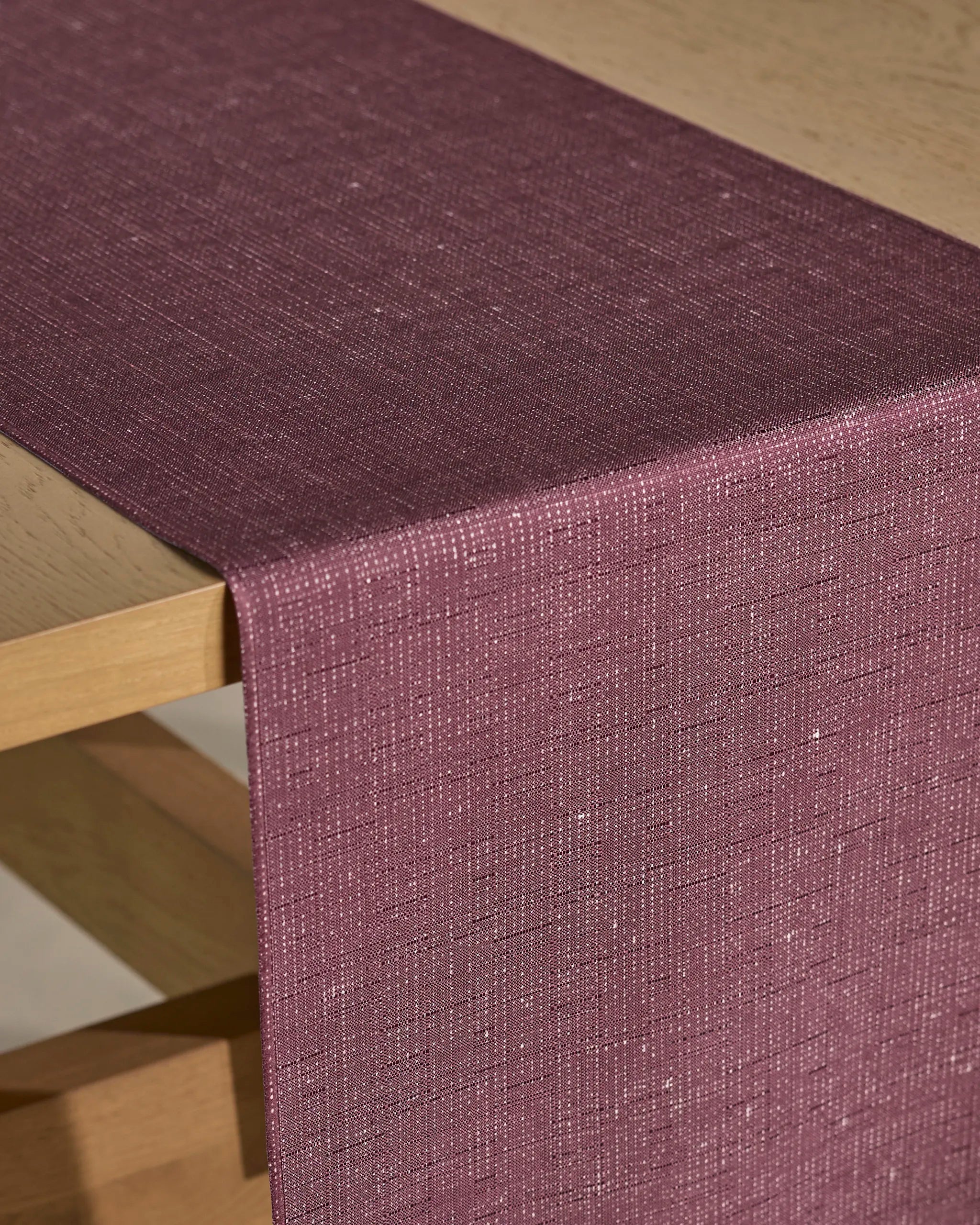 A close-up of a wooden table with the Geometry Gather table runner in deep mauve, featuring a stain-resistant finish and subtle shimmering woven pattern, elegantly draped across it.
