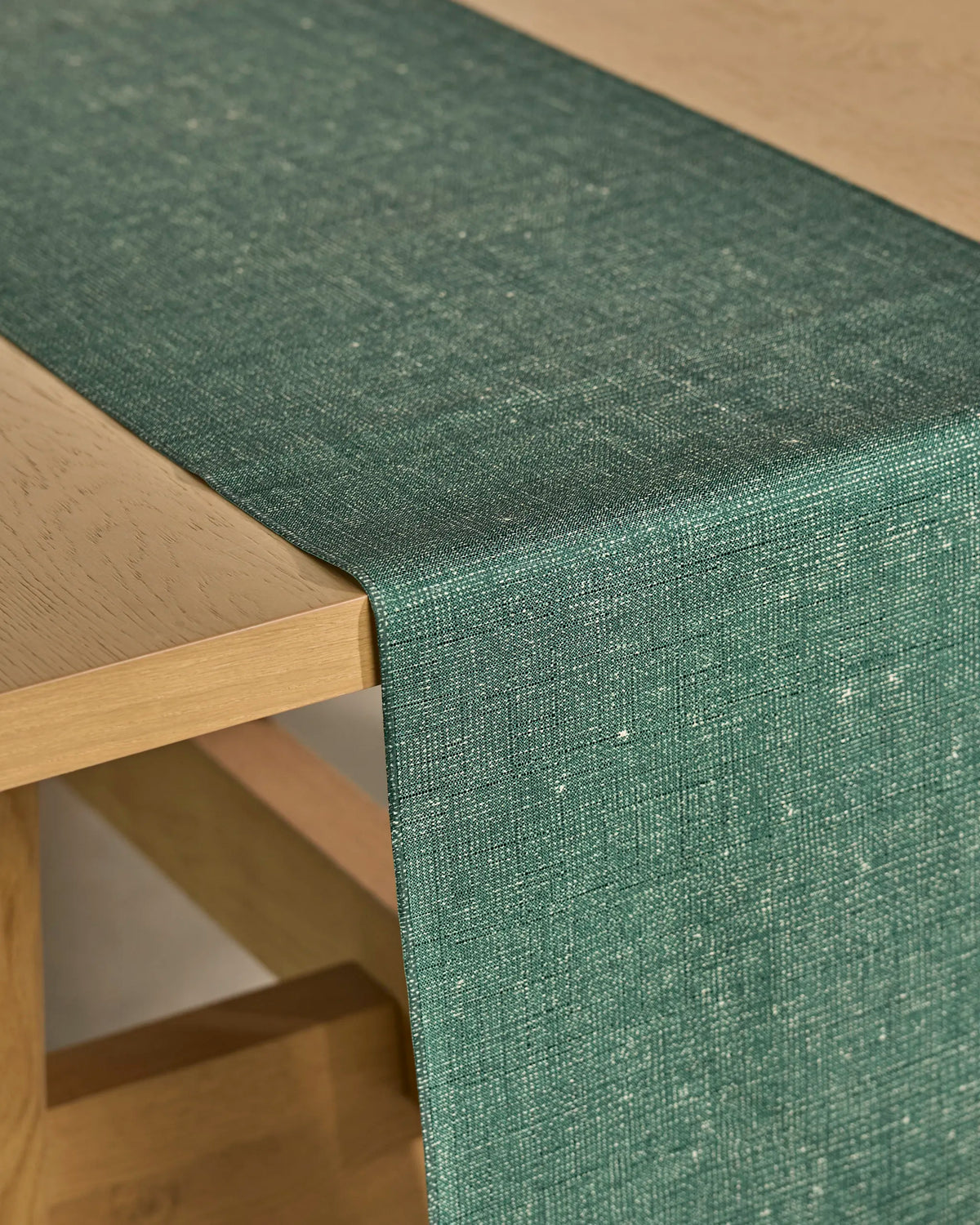 A close-up of a light wooden table with the “Gather” green textured recycled table runner by Geometry draped over the edge.
