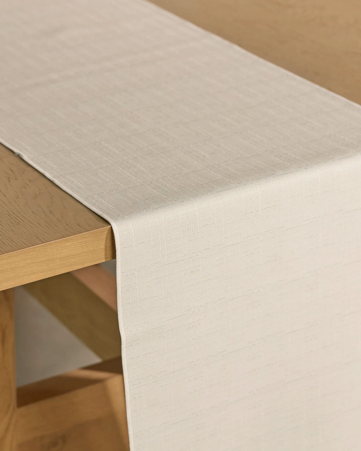 A Geometry Gather table runner in beige, crafted from textured, stain-resistant fabric, is draped neatly over the edge of a light wooden table.