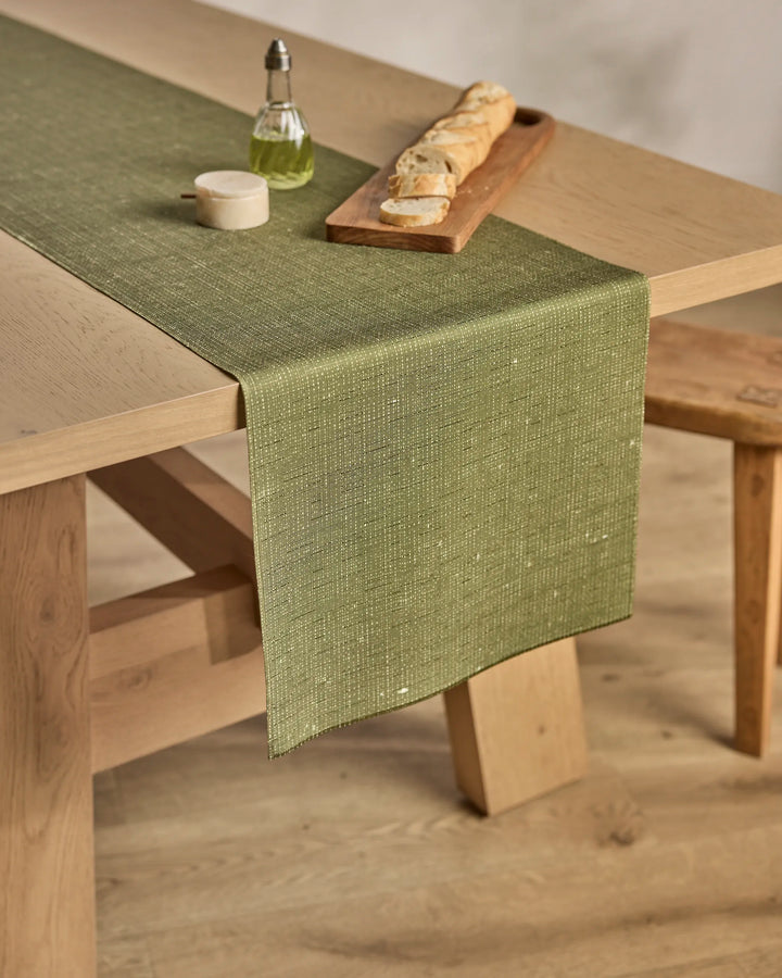 A table featuring a Geometry Willa Green stain-resistant table runner and a tray of bread.