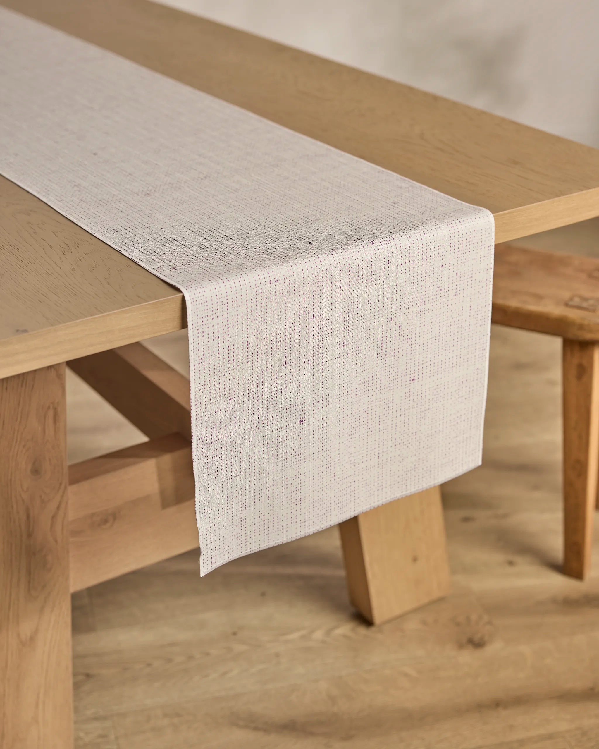 The Willa Lav table runner by Geometry, in light beige and stain-resistant, is elegantly placed on a wooden dining table with matching benches atop a light wood floor.