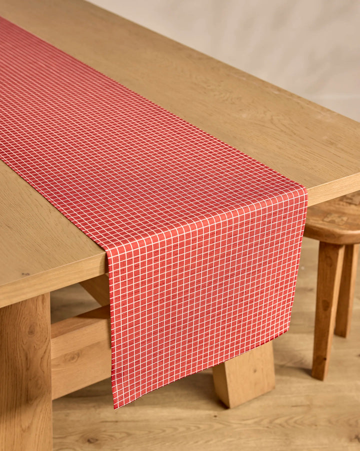 A table with the Candy Cane Grid red, stain-resistant table runner by Kailee Wright.