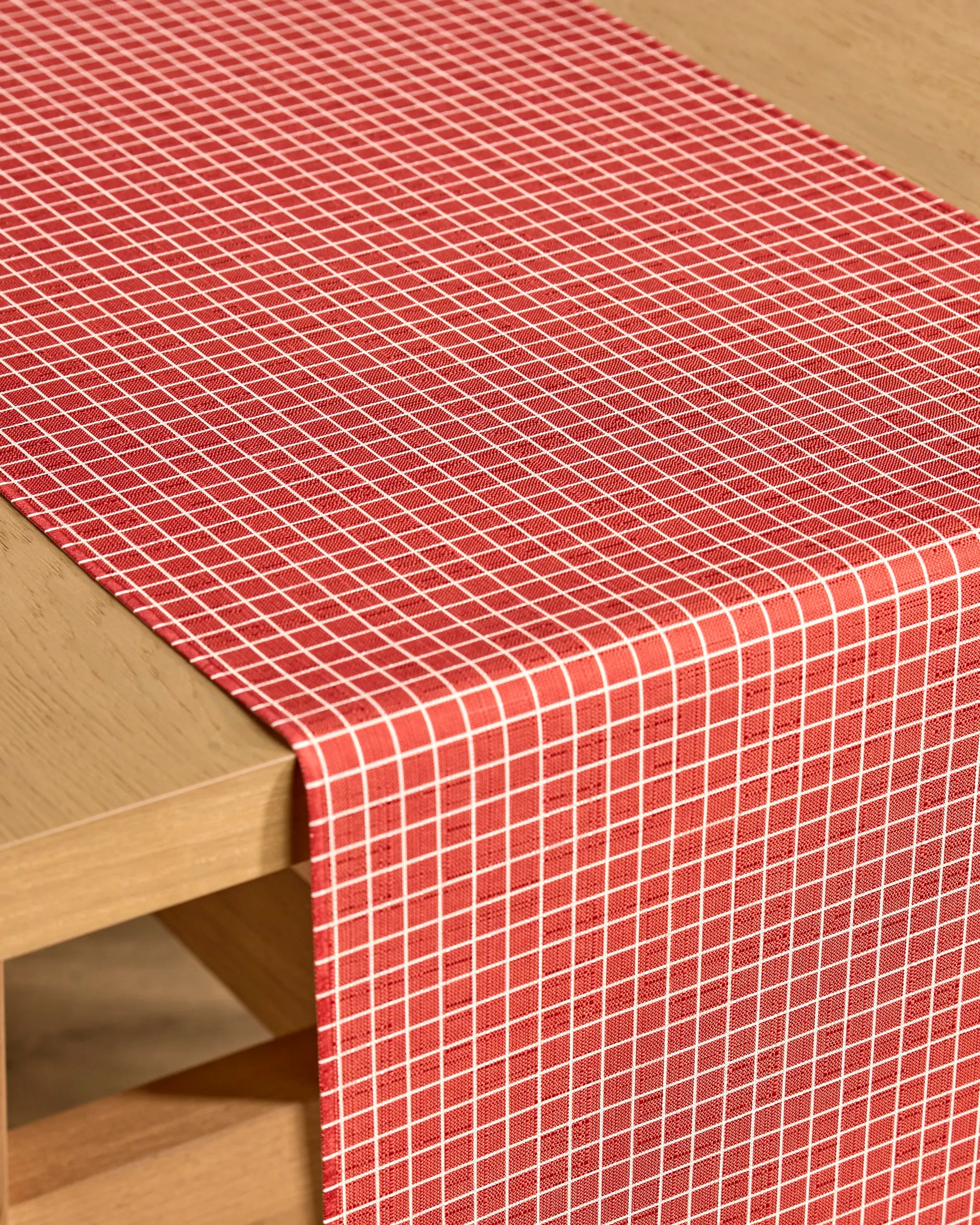 The Kailee Wright "Candy Cane Grid" table runner features a precise red and white small-square pattern, neatly laid across a light wooden table.