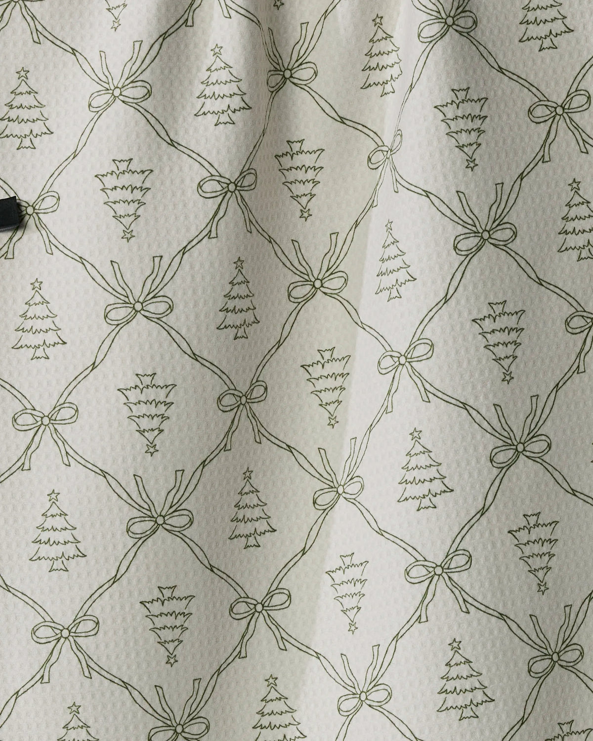 Bring festive charm to your kitchen with the “Cedar Bows” tea towel from Geometry. This white quick-drying towel features a repeating pattern of hand-drawn green Christmas trees and bows arranged in a diamond grid, while light shadows accent gentle folds—making it both stylish and practical for everyday use.