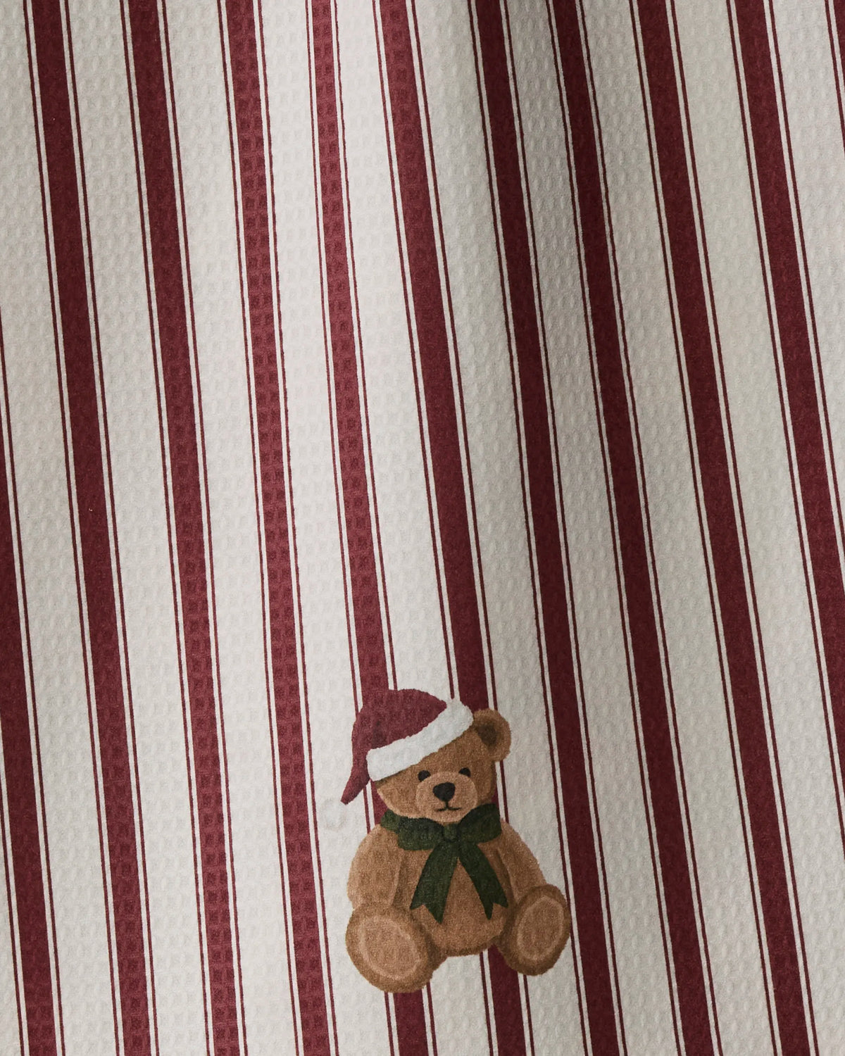 The Geometry “Christmas Bear” tea towel features red and white vertical stripes and a charming illustration of a brown teddy bear in a red Santa hat and green scarf near the bottom, crafted double-sided for enhanced versatility.