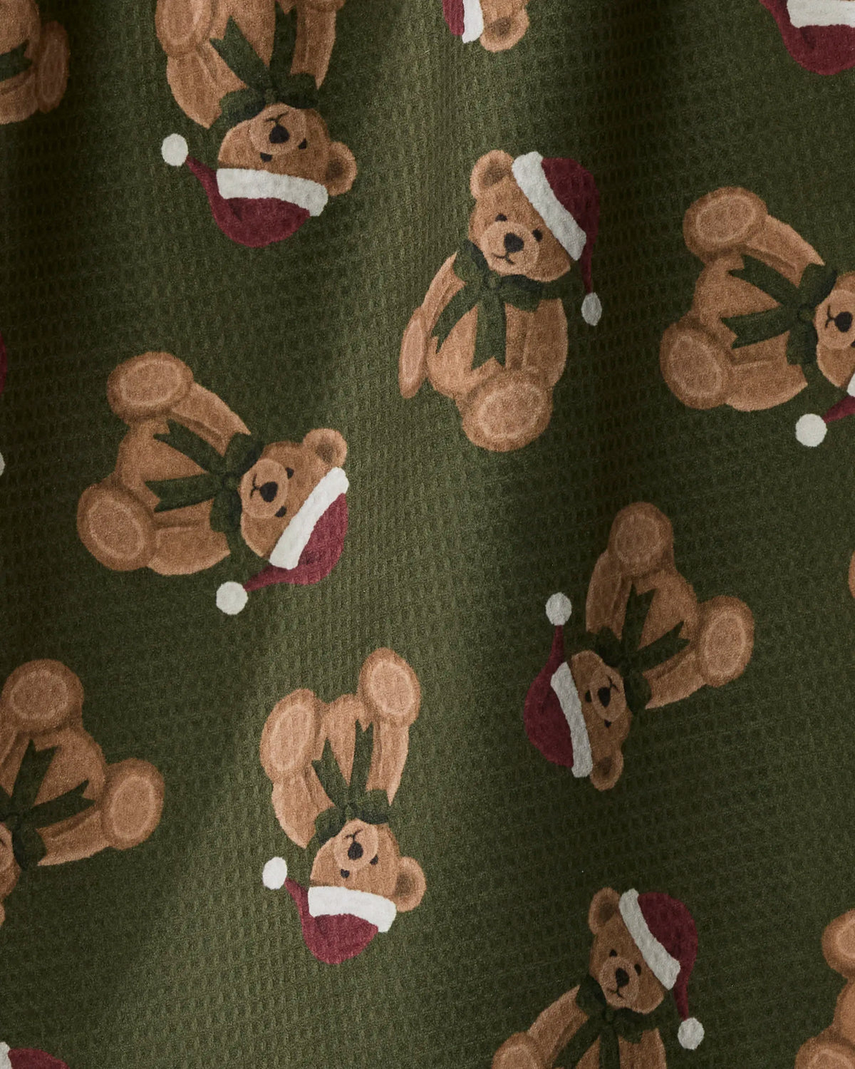 Geometry’s “Christmas Bear” features a green, textured fabric made from recycled materials, adorned with a repeating pattern of brown teddy bears wearing red Santa hats and green scarves in various positions.