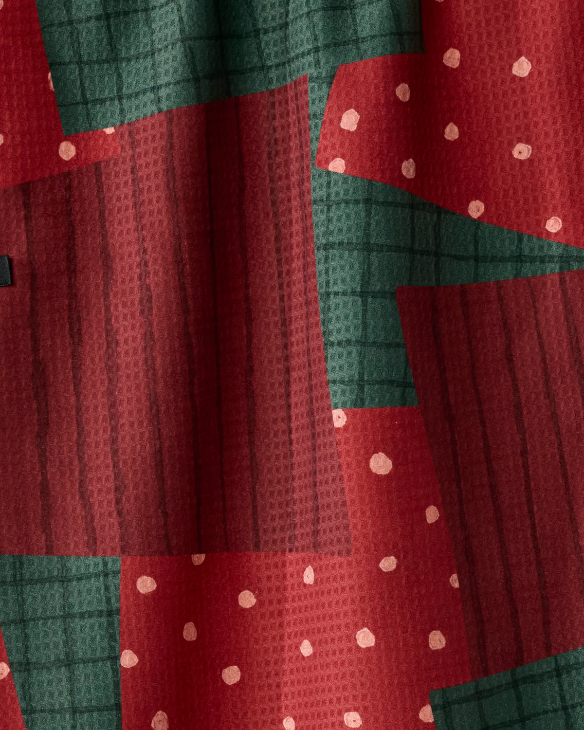 Christmas Crafts by Geometry showcases a red and green fabric with a patchwork design of solid and striped rectangles, accented by scattered white polka dots. Made from recycled materials, the fabric has a textured appearance and drapes softly in gentle folds.