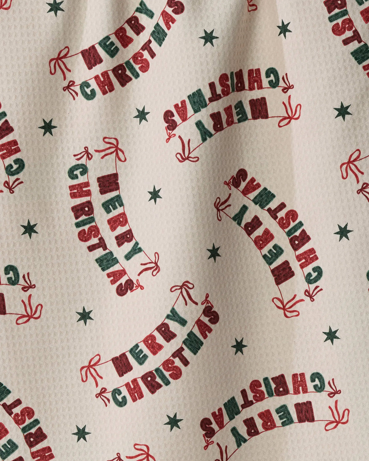 Introducing Christmas Crafts by Geometry: a cream-colored, quick-drying fabric crafted from recycled materials, showcasing green stars and red “Merry Christmas” text in a curved banner pattern repeated across the surface.
