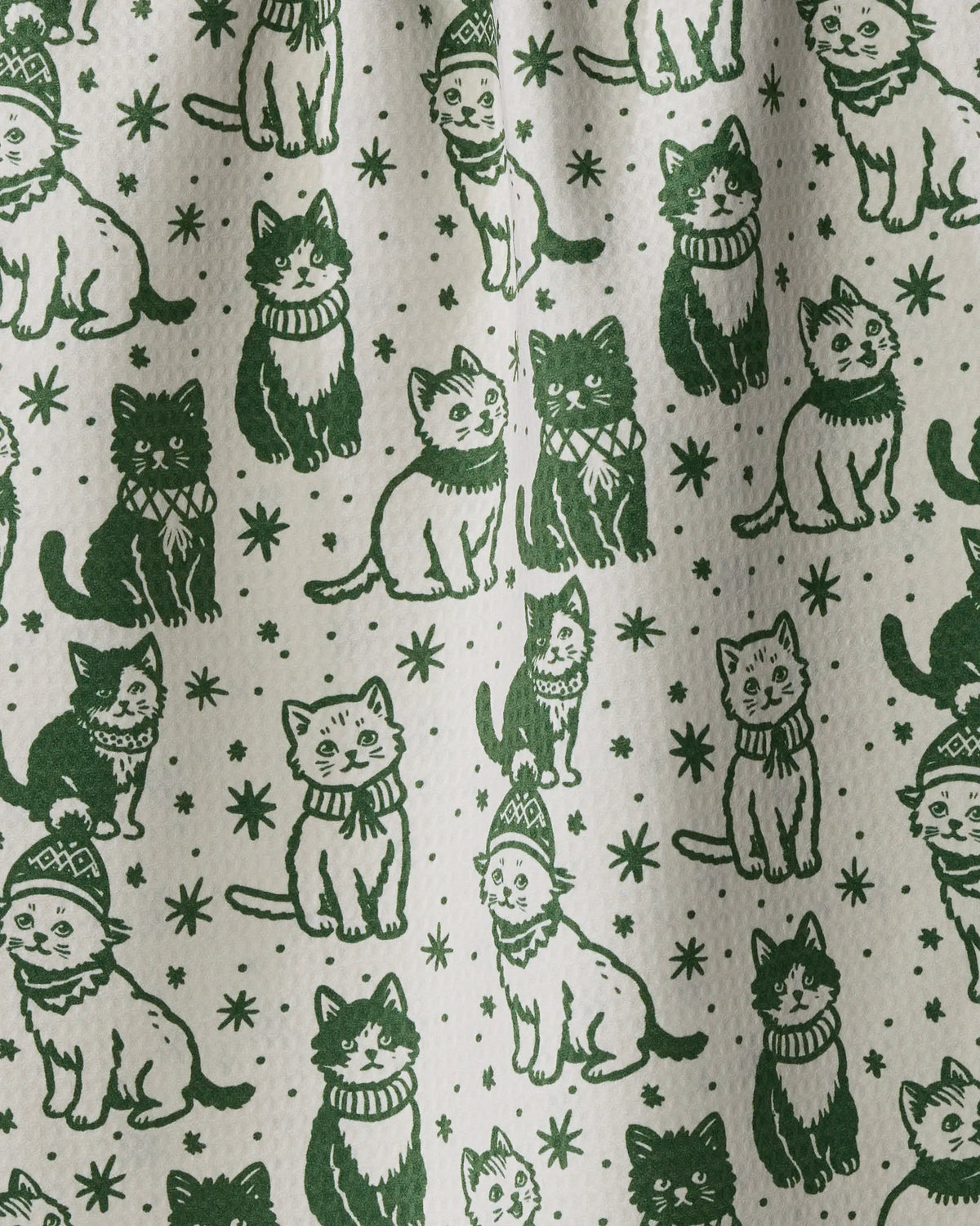 The Cozy Kittens tea towel by Geometry features a double-sided design with green illustrated cats in scarves and hats, playfully posed among stars and dots on a white background. This quick-drying tea towel offers both charm and practicality for any kitchen.