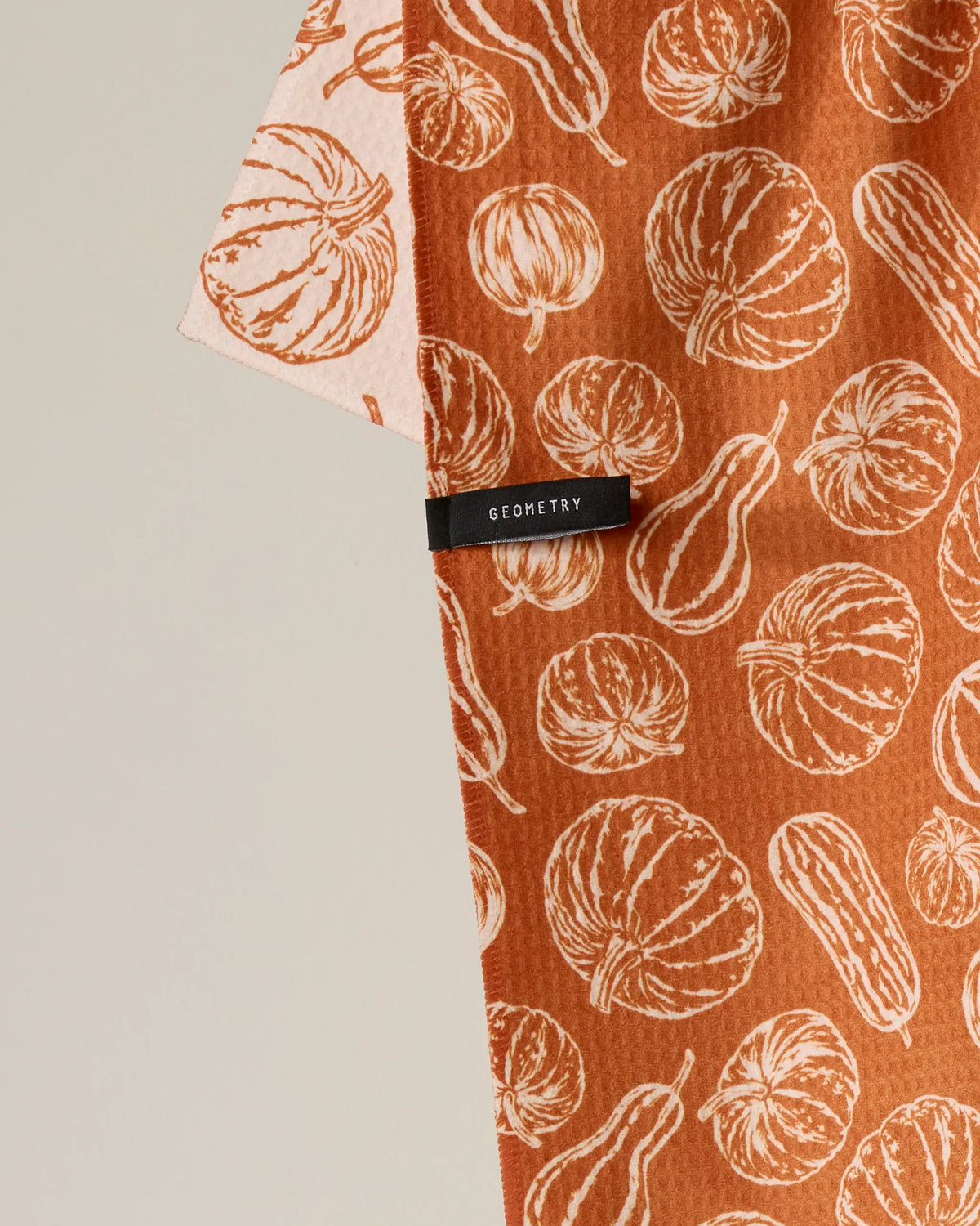 Introducing “Harvest Sketch” by Geometry: a quick-drying, double-sided tea towel in orange and beige hues, adorned with illustrated pumpkin and squash motifs and finished with a black GEOMETRY label—thoughtfully made from recycled materials.