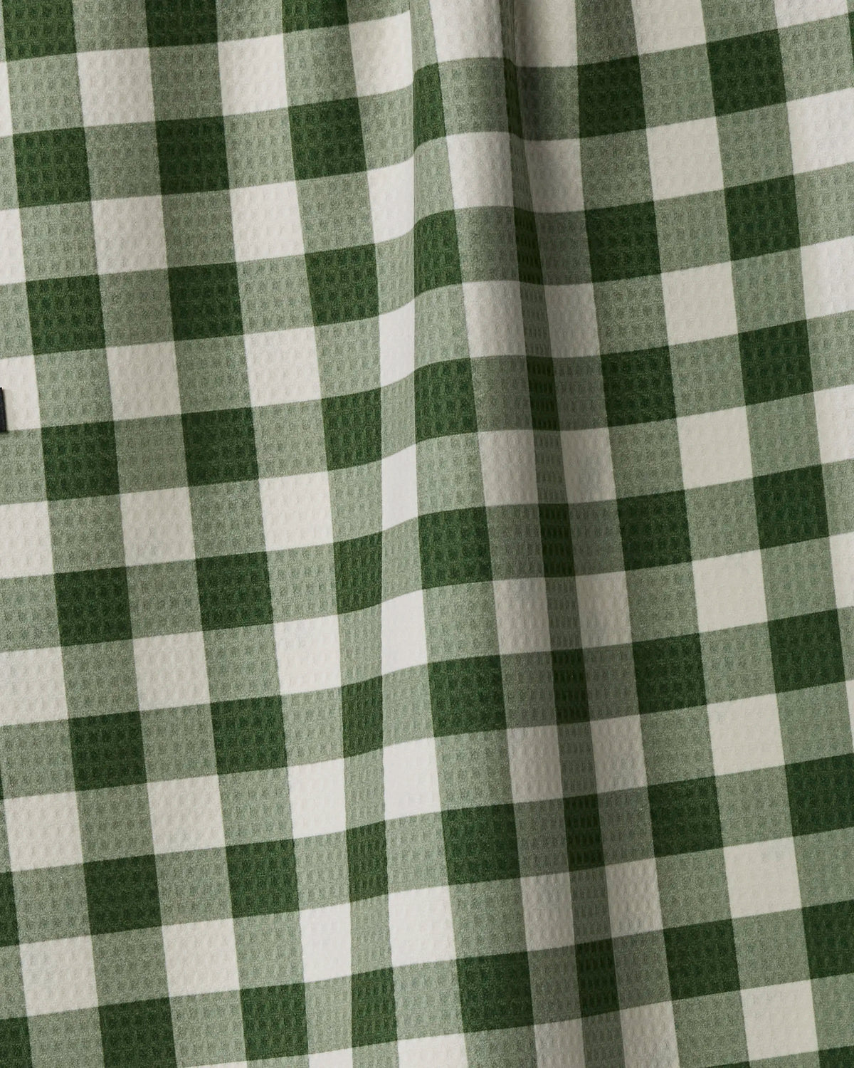 Holiday Holly by Geometry is a green and white checkered fabric with a textured surface, crafted from recycled materials and featuring visible folds that create subtle shadows.
