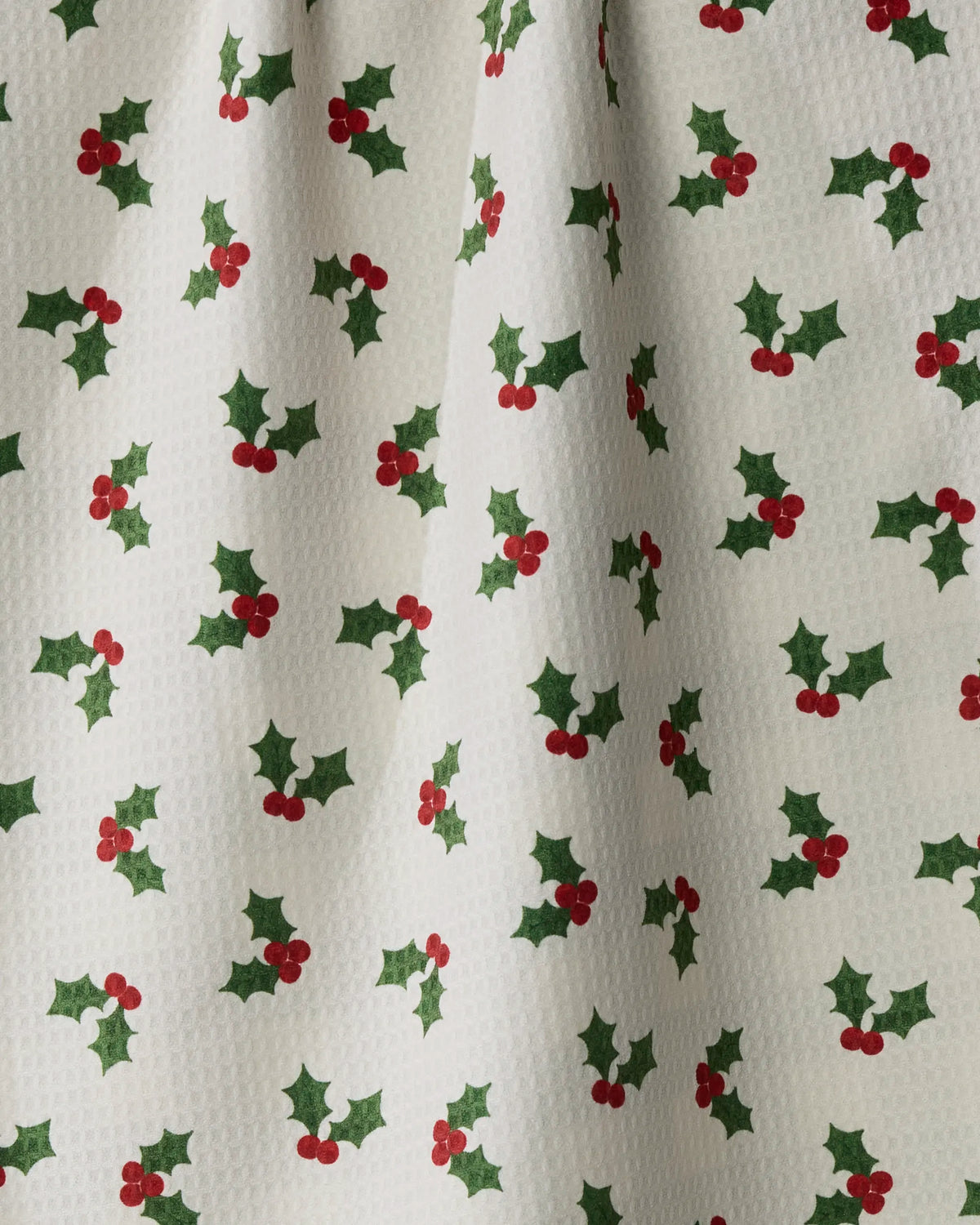 Introducing the Holiday Holly tea towel by Geometry: Featuring a white textured fabric adorned with green holly leaves and red berries, this festive, holiday-themed design is crafted from recycled materials. Double-sided for versatility, this absorbent and quick-drying tea towel is both eco-friendly and perfect for seasonal celebrations.