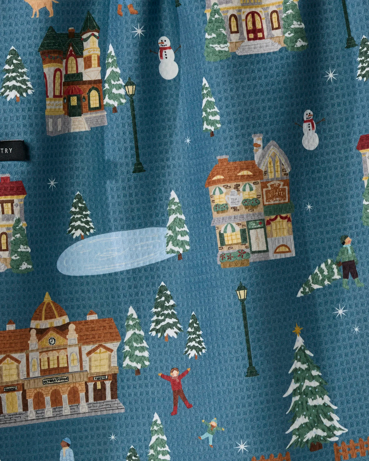 Holiday Nostalgia by Geometry features a beautifully crafted double-sided tea towel adorned with winter village scenes—houses, snowmen, evergreen trees, street lamps, an ice skating rink, and people in cozy winter attire—all set against a blue background, bringing festive charm to your kitchen décor.