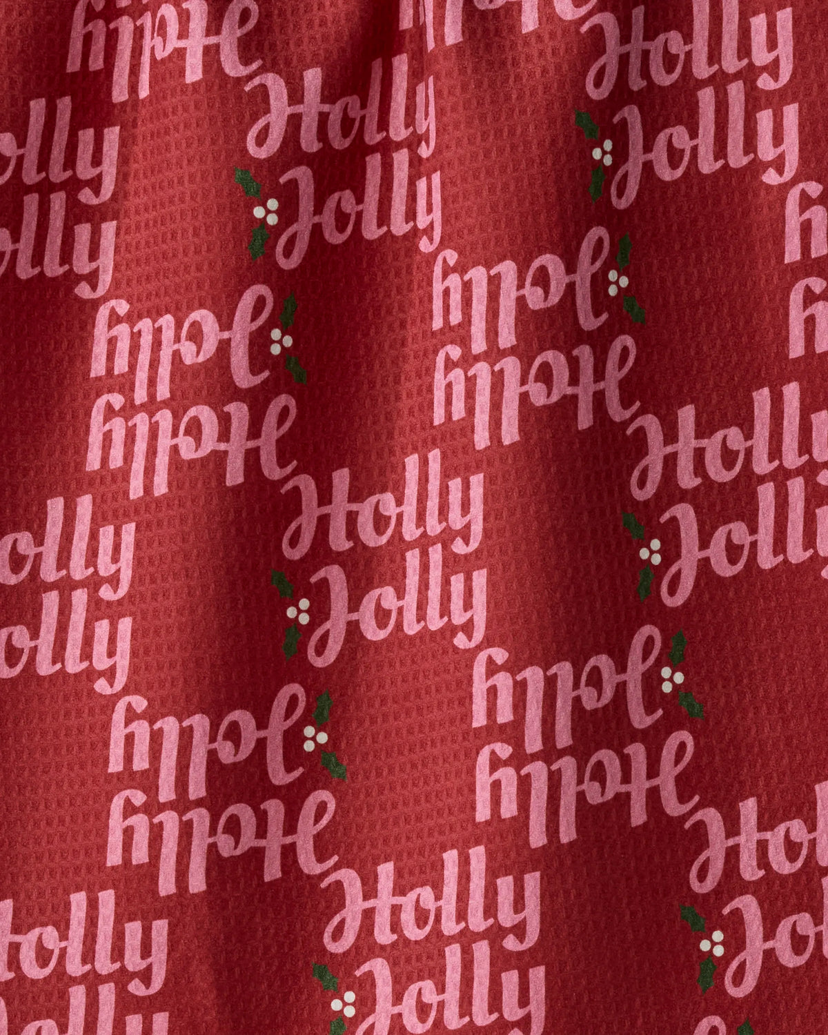 The Geometry Holly Jolly Xmas kitchen towel features a red fabric adorned with repeating “Holly Jolly” text in white, complemented by green holly leaves and red berries arranged both upright and upside down throughout the pattern. Made from recycled materials, this absorbent towel is an eco-friendly and festive choice for your holiday décor.