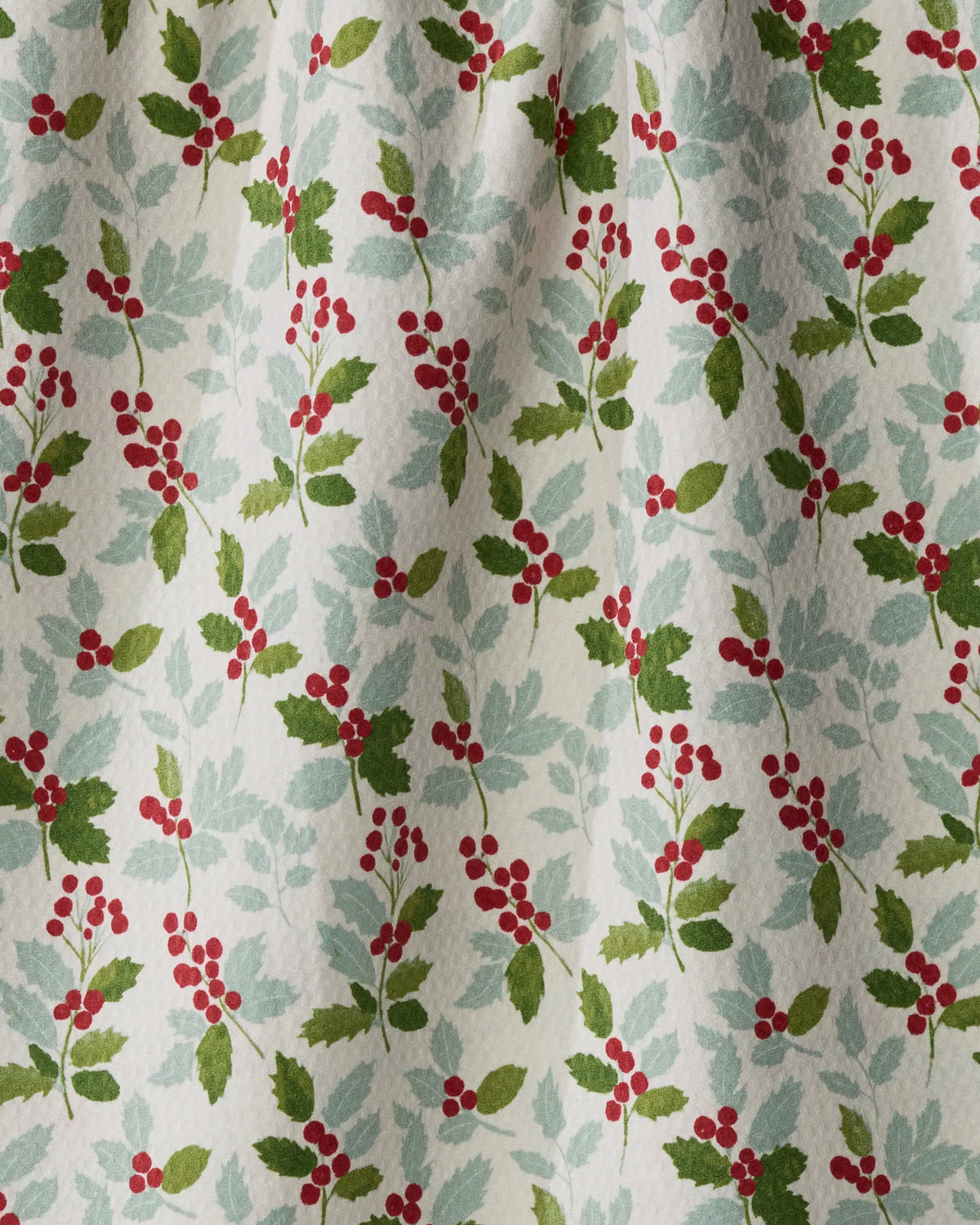 The Geometry “Holly Lane” tea towel features a festive pattern of green holly leaves and red berry clusters on a crisp white background. Made from recycled materials, this quick-drying, double-sided towel adds sustainable seasonal charm to your kitchen.