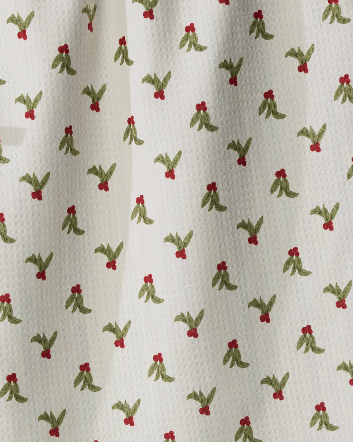 Introducing Holly Vine by Geometry—this double-sided tea towel features a white textured fabric adorned with an evenly spaced repeating pattern of small green holly-like leaves and clusters of three red berries. Crafted from quick-drying recycled materials, it brings both eco-friendly style and lasting practicality to your kitchen.