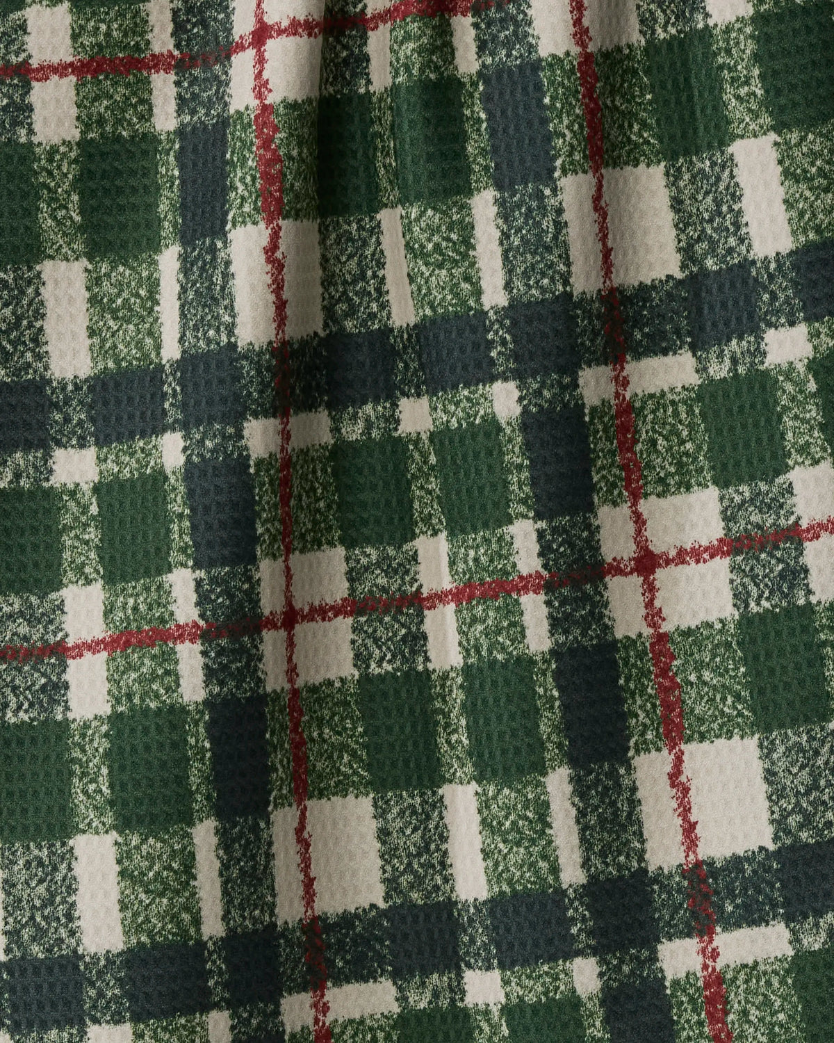 A close-up of Juniper Plaid fabric by Geometry showcases its green, red, and white plaid pattern with a textured, waffle-like surface and soft folds—crafted from recycled materials for an eco-friendly touch.