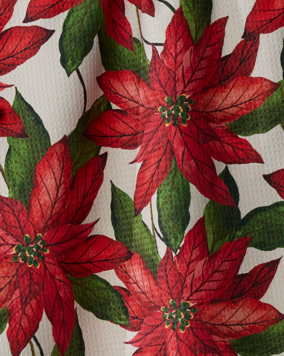 Introducing the Lauri tea towel by Geometry — featuring vivid red poinsettia blooms with lush green leaves printed on textured white fabric. This vibrant, festive pattern extends across both sides of the towel, capturing a perfect holiday spirit. Both stylish and practical, this double-sided piece is an elegant addition to your kitchen décor.