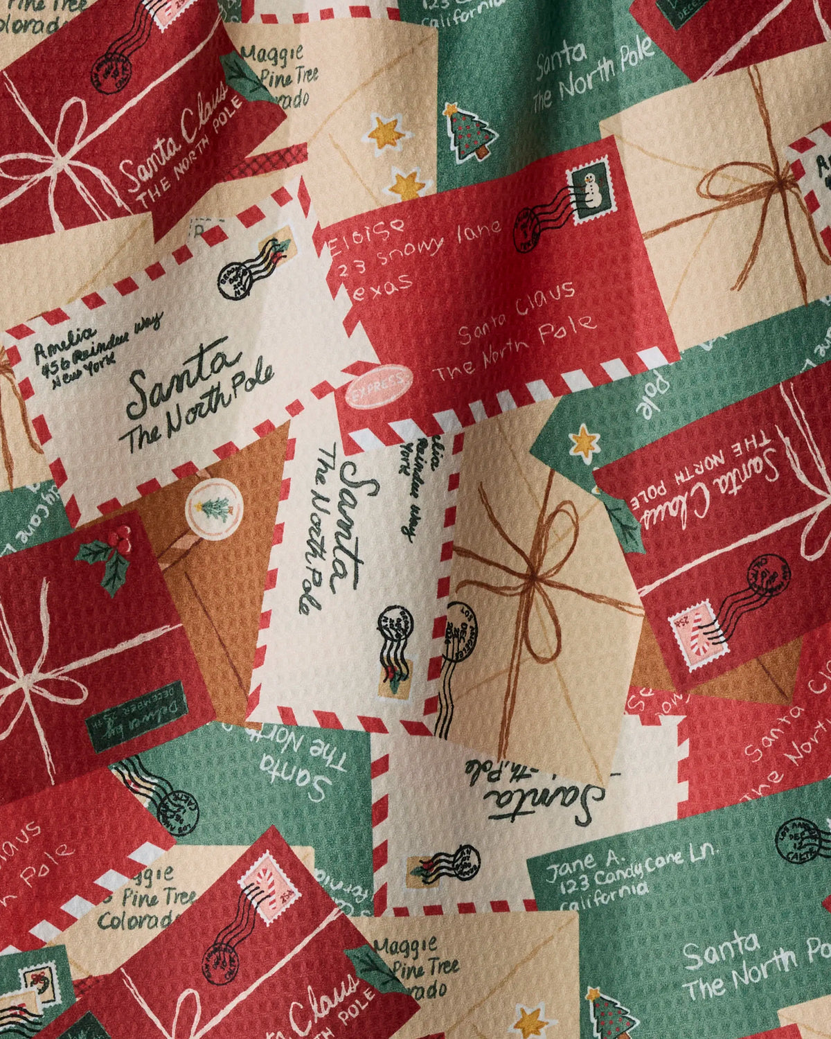 A close-up of festive envelopes and postcards with holiday-themed stamps and addresses to Santa at the North Pole overlap in a vibrant, textured pattern—perfectly capturing the cheerful spirit of the season, just like Geometry’s Merry Mail quick-drying tea towel brings both function and style to your kitchen.