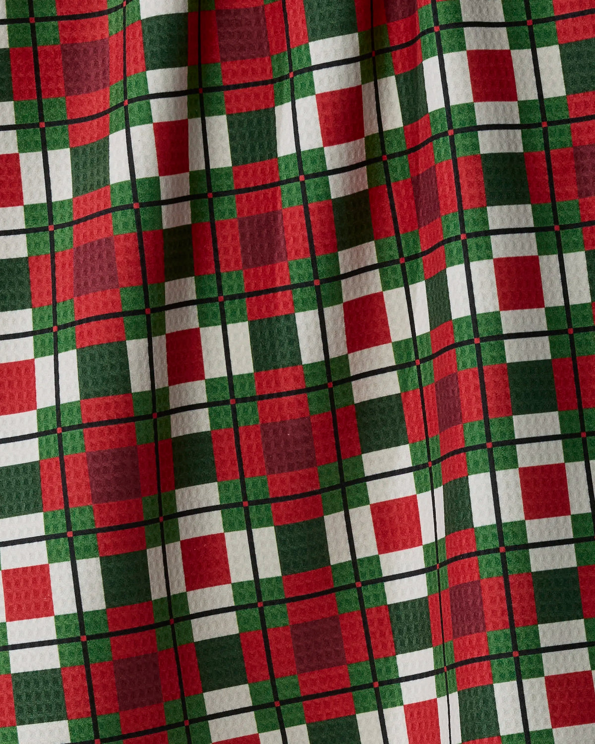Introducing Noel Plaid by Geometry—a checkered fabric in red, green, white, and black with a textured, slightly crinkled finish. The evenly spaced pattern evokes festive holiday charm—ideal for creating a double-sided tea towel made from recycled materials.