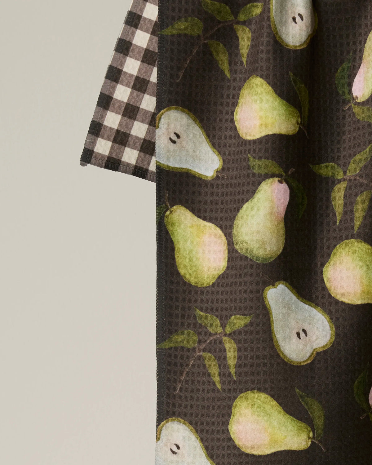 The Geometry Pearwood tea towel features a double-sided design with a vibrant watercolor pear pattern in green and pink, artfully paired with a black and white checkered sleeve set against a plain background. Crafted from absorbent, quick-drying material, Pearwood is both stylish and practical for everyday use.