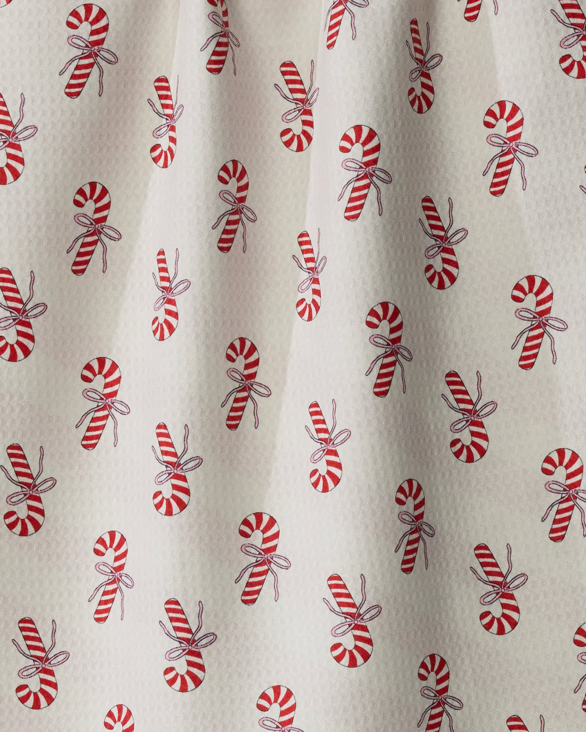 Peppermint Lane by Geometry features a festive white fabric adorned with evenly spaced red and white candy canes and round peppermint candies, each accented with a small bow. Crafted as a quick-drying tea towel, this charming design adds both holiday cheer and practical function to your kitchen.