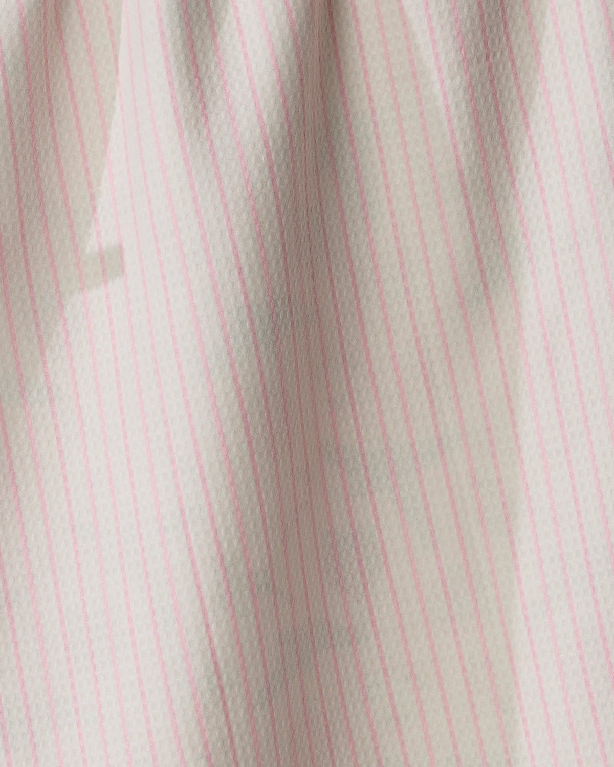 A close-up of Geometry’s Pink Tidings tea towel, crafted from recycled materials, showcasing its double-sided design with white fabric and thin vertical pink stripes; subtle shadows enhance the softly textured, quick-drying look.