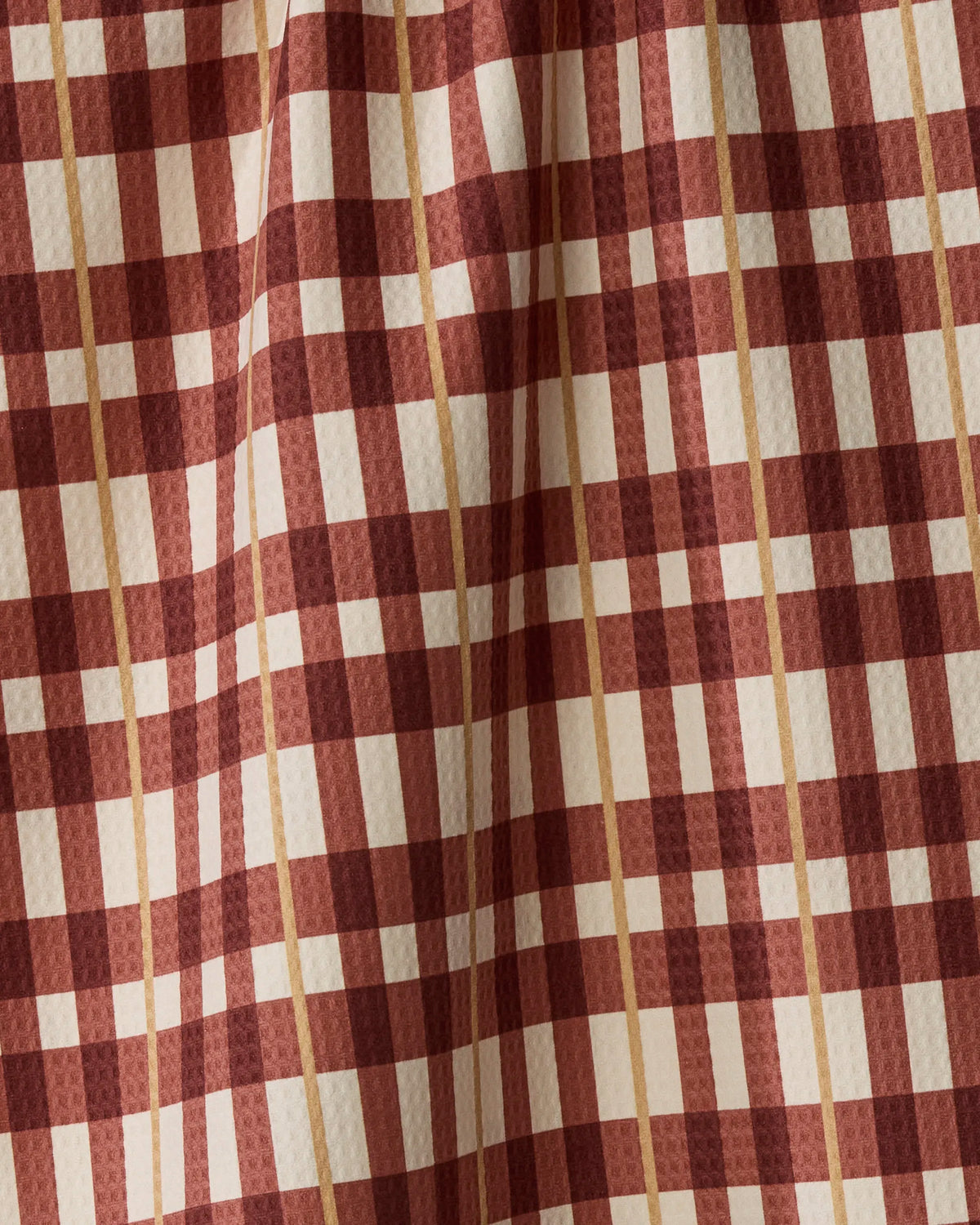 A close-up of Plaid Teddy by Geometry showcases its red and beige plaid fabric, where vertical and horizontal lines intersect with subtle folds for added texture—making this absorbent, quick-drying towel a stylish yet highly functional choice.