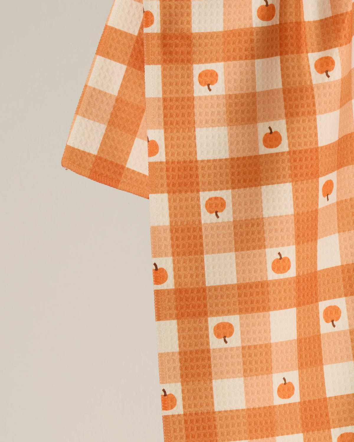 Introducing the “Pumpkin Check” tea towel by Geometry: this double-sided kitchen essential features an orange and white checkered pattern adorned with small pumpkin illustrations, combining charming design with practical functionality for your home.