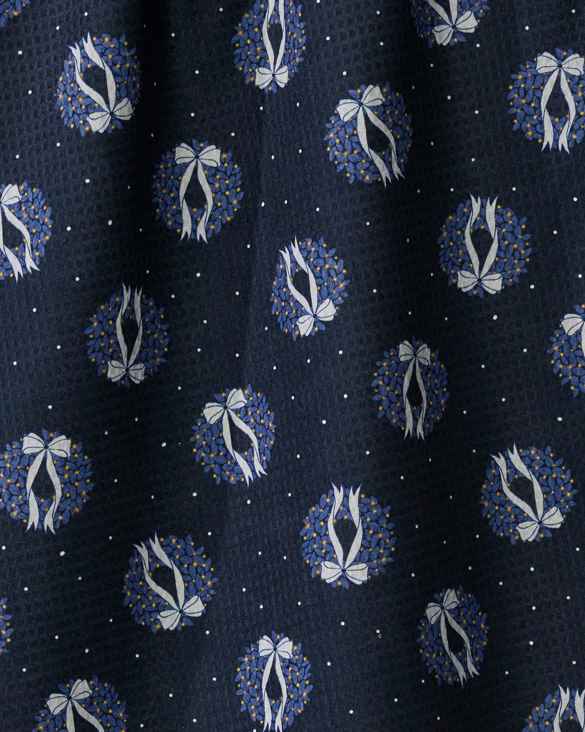 Introducing Geometry’s Quiet Skies tea towel—a double-sided, dark fabric towel featuring a repeating pattern of blue wreaths tied with white bows, spaced with small white dots on a textured background. Absorbent and quick-drying, Quiet Skies combines stylish design with everyday kitchen practicality.