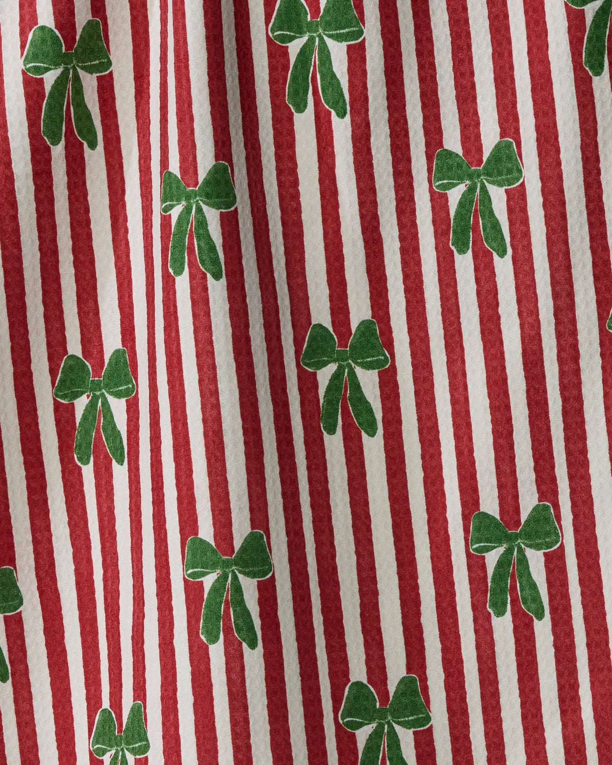 The “Ribbon Bows” double-sided tea towel by Geometry features red and white vertical stripes accented with a repeating pattern of green bows on a textured fabric surface, creating a charming and stylish design. Crafted from recycled materials, this absorbent, quick-drying towel is as practical as it is attractive.