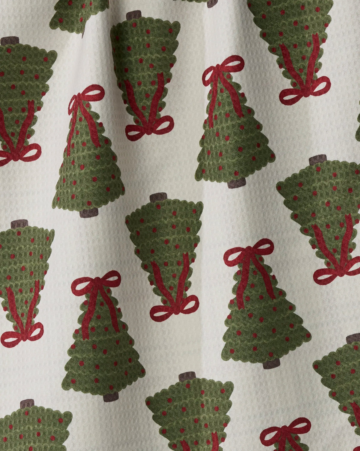 The Geometry Ribbon Pines towel features a festive design of green Christmas trees adorned with red ornaments and bows, printed on white textured fabric. Made from recycled materials, this quick-drying and absorbent towel combines sustainability with holiday cheer.
