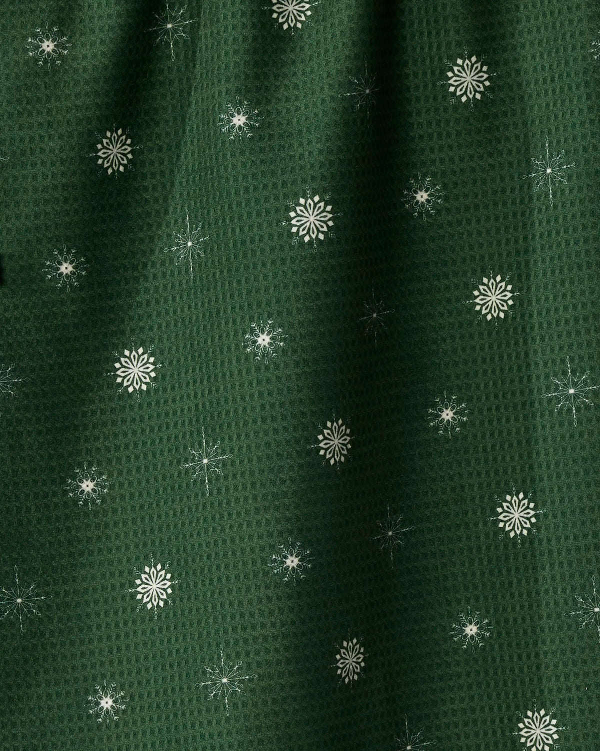 The Geometry Snowflake Chalet tea towel features a dark green fabric with a textured pattern, adorned with small white snowflakes and starburst shapes evenly distributed across its double-sided surface. Both stylish and practical, it adds a festive touch to your kitchen essentials.