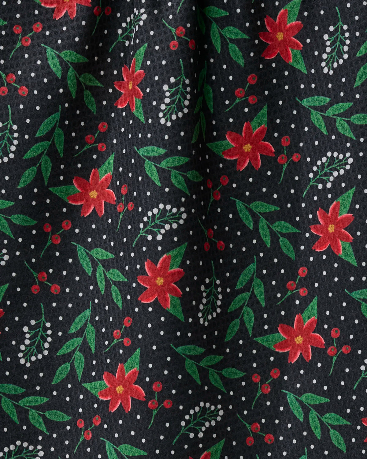 Winter Bloom by Geometry features a festive black fabric adorned with red flowers, green leaves, white dots, and small white berries. Crafted from recycled materials, this double-sided tea towel is eco-friendly and stylish—perfect for adding decorative flair to any kitchen space.
