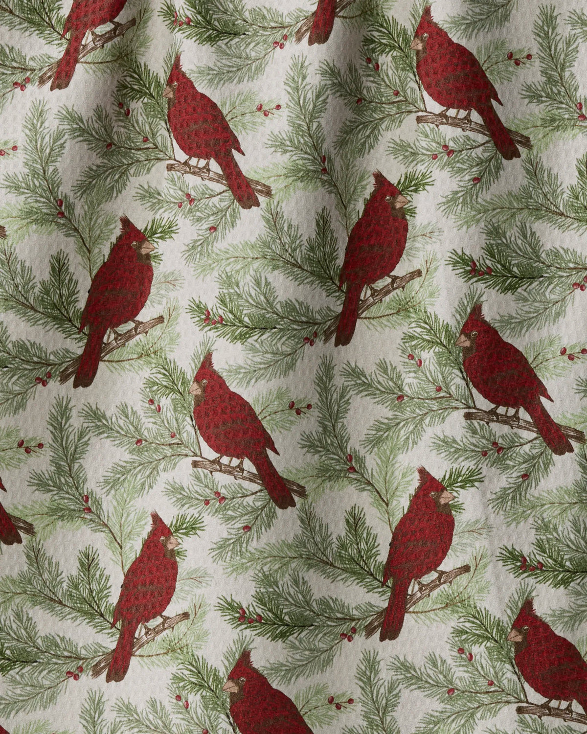 Winter Crimson by Geometry features a pattern of red cardinals perched on pine branches with green needles and red berries set against a light background. This double-sided tea towel combines charming seasonal design with practical versatility for your kitchen, crafted from fabric that appears slightly wrinkled for added character.